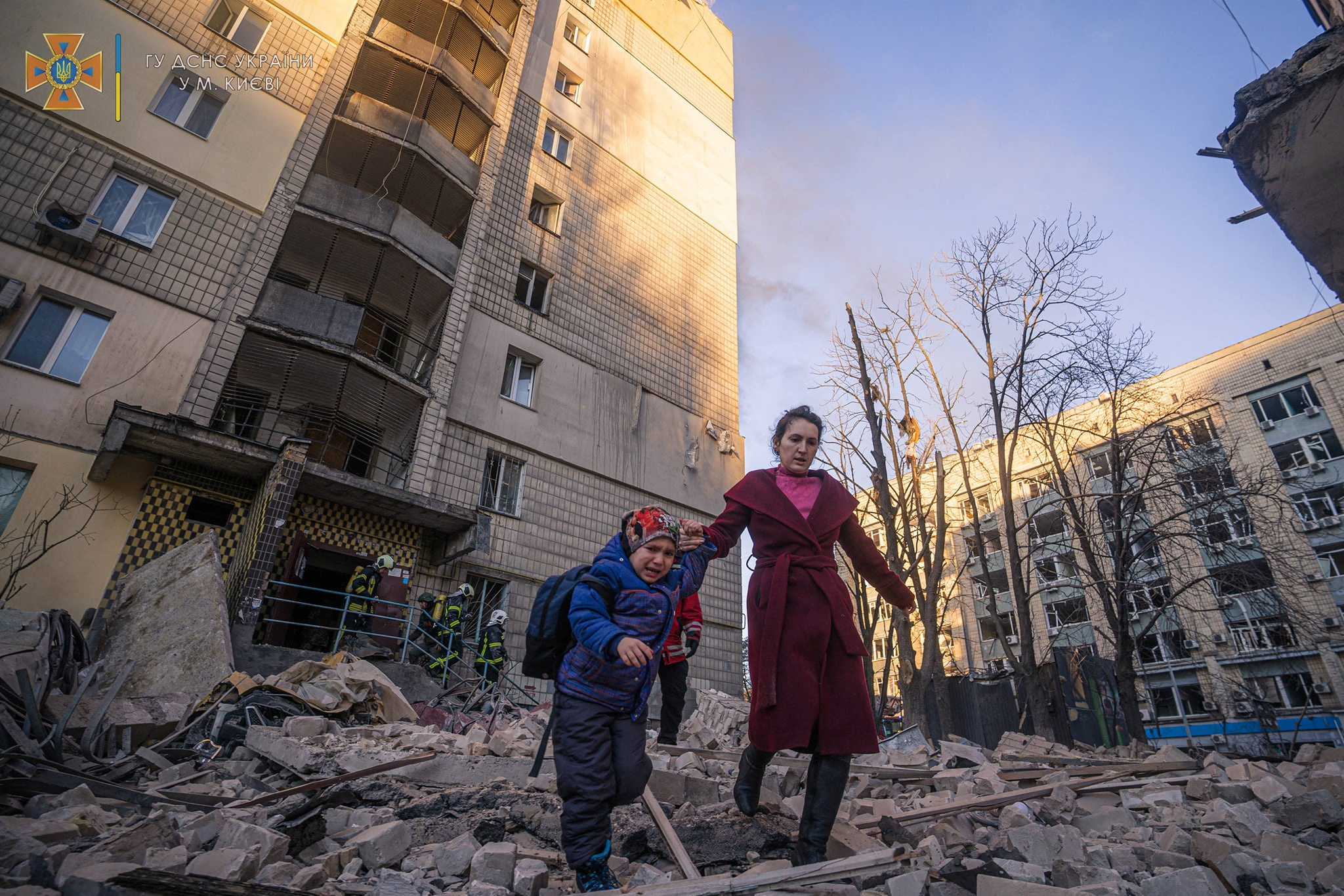 A woman with a child evacuates from a residential building damaged by shelling in Kyiv
