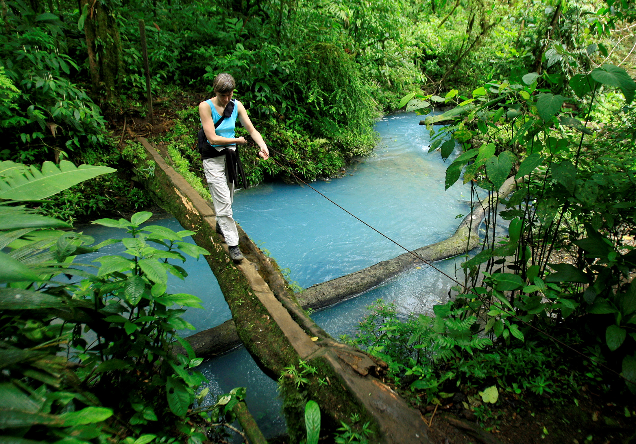 A Spanish tourist crosses a bridge over the Celeste river at Tenorio Volcano National Park in Upala March 18, 2008. The blue color of the lagoon, formed from chemical reactions of calcium carbonate and sulfur, is surrounded by an amazing rainforest that constitutes 12,819 hectares of this park. REUTERS/Juan Carlos Ulate (COSTA RICA)