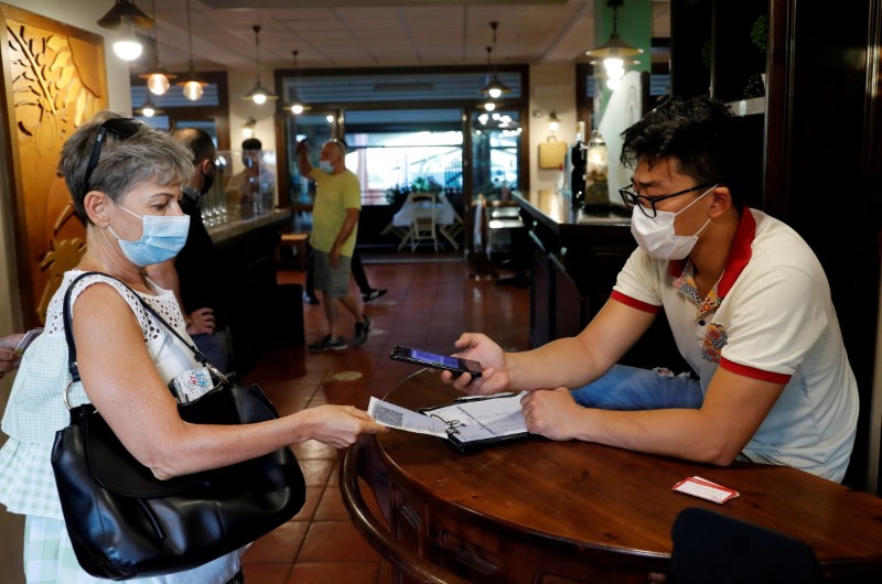 A woman has her Green Pass (health pass) checked before entering a pizzeria as Italy brings in tougher restrictions where a proof of immunity will be required to access an array of services and leisure activities, in Rome, Italy, August 6, 2021. REUTERS/Remo Casilli/File Photo