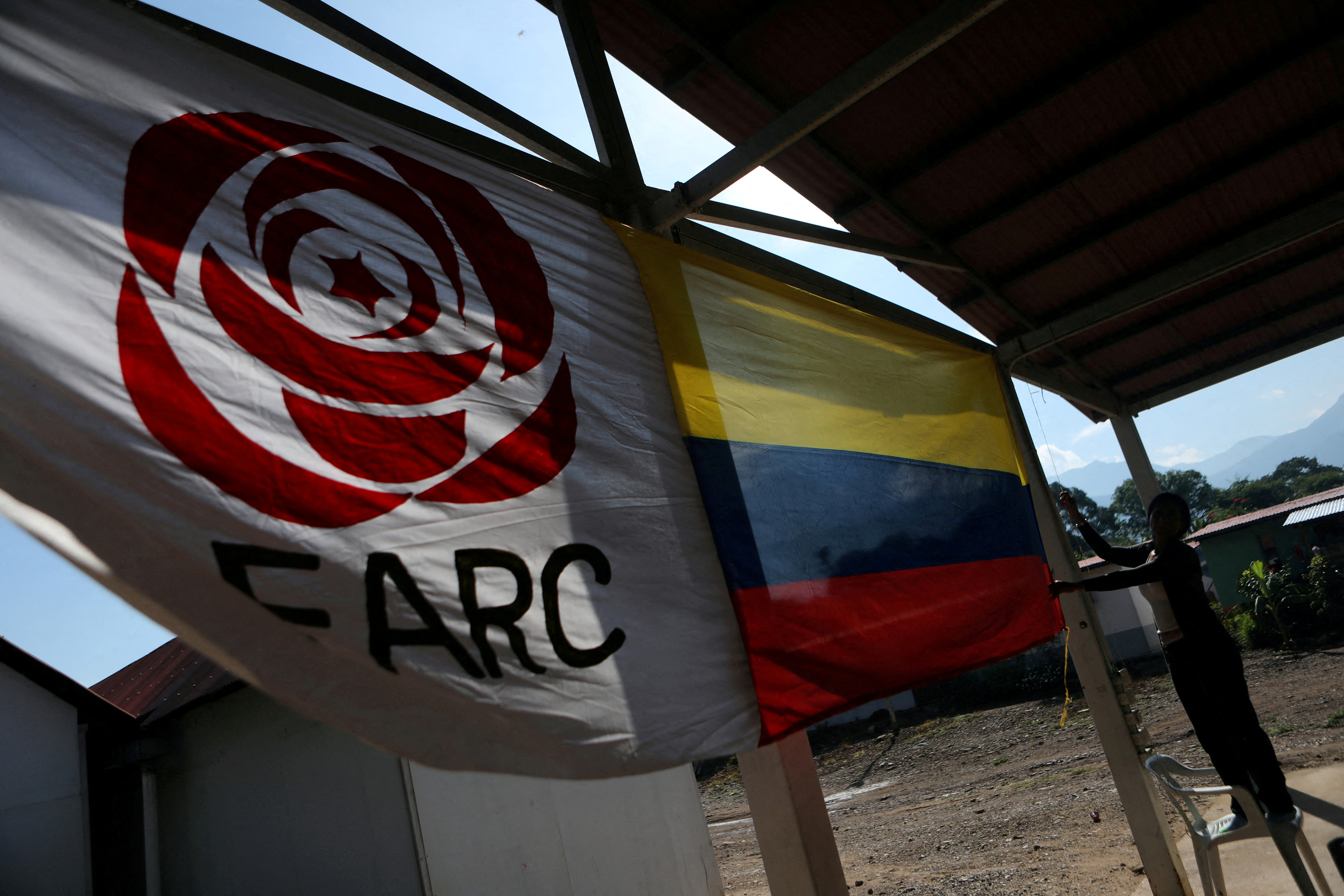 A woman hangs a Colombian flag next to the Revolutionary Alternative Force of the Common (FARC) Political party flag at a reintegration camp in Pondores
