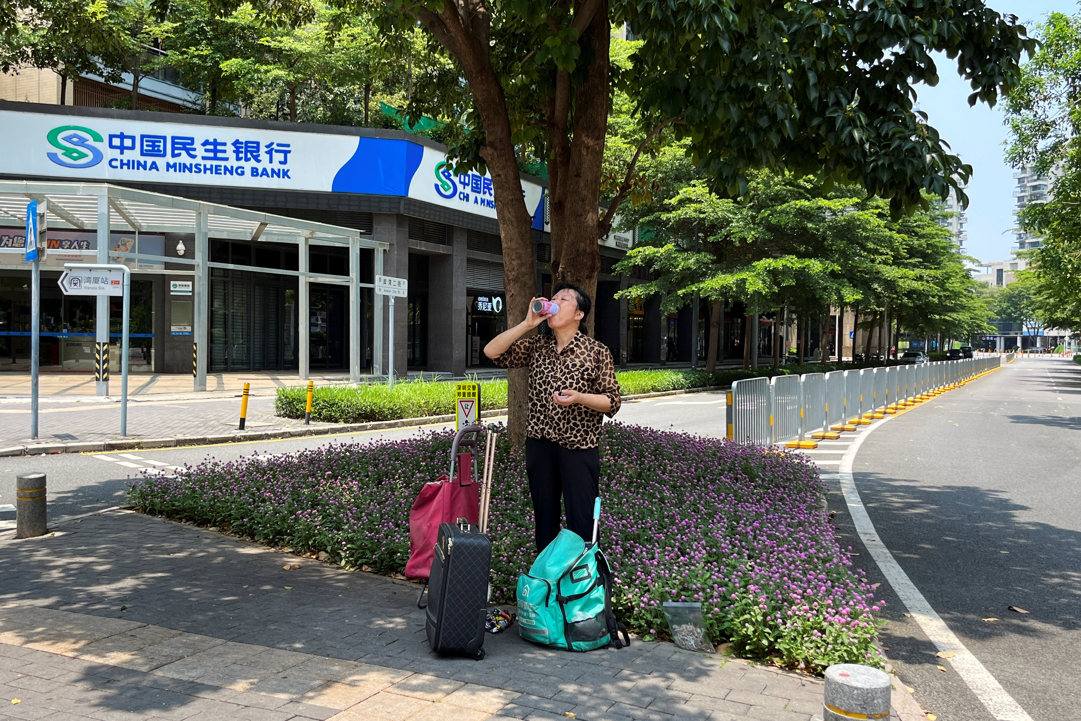 A woman standing under a tree drinks from a can amid a yellow alert for heatwave in Shenzhen
