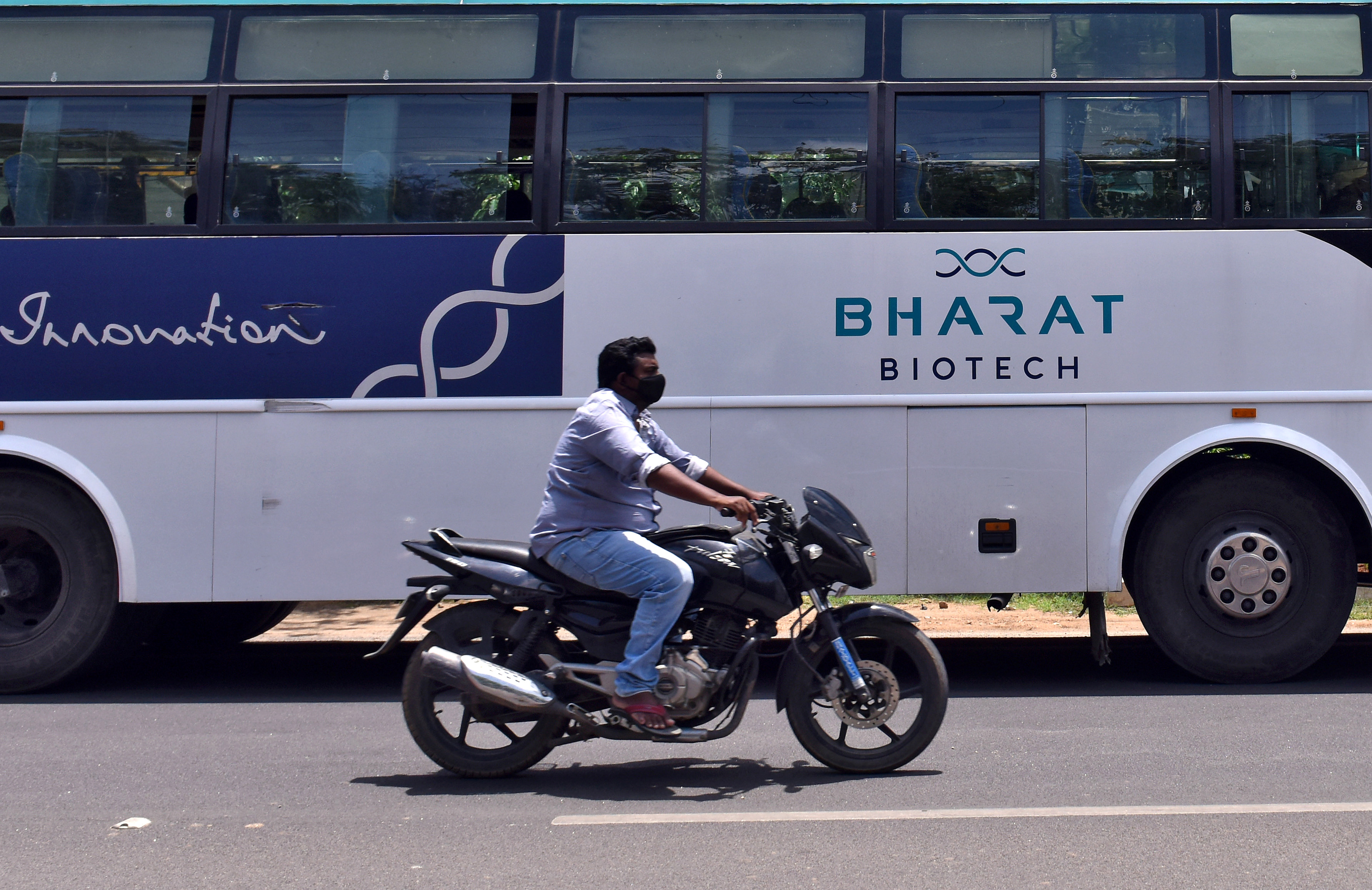 A man rides his motorbike past a parked bus of India's biotechnology company Bharat Biotech outside its office in Hyderabad