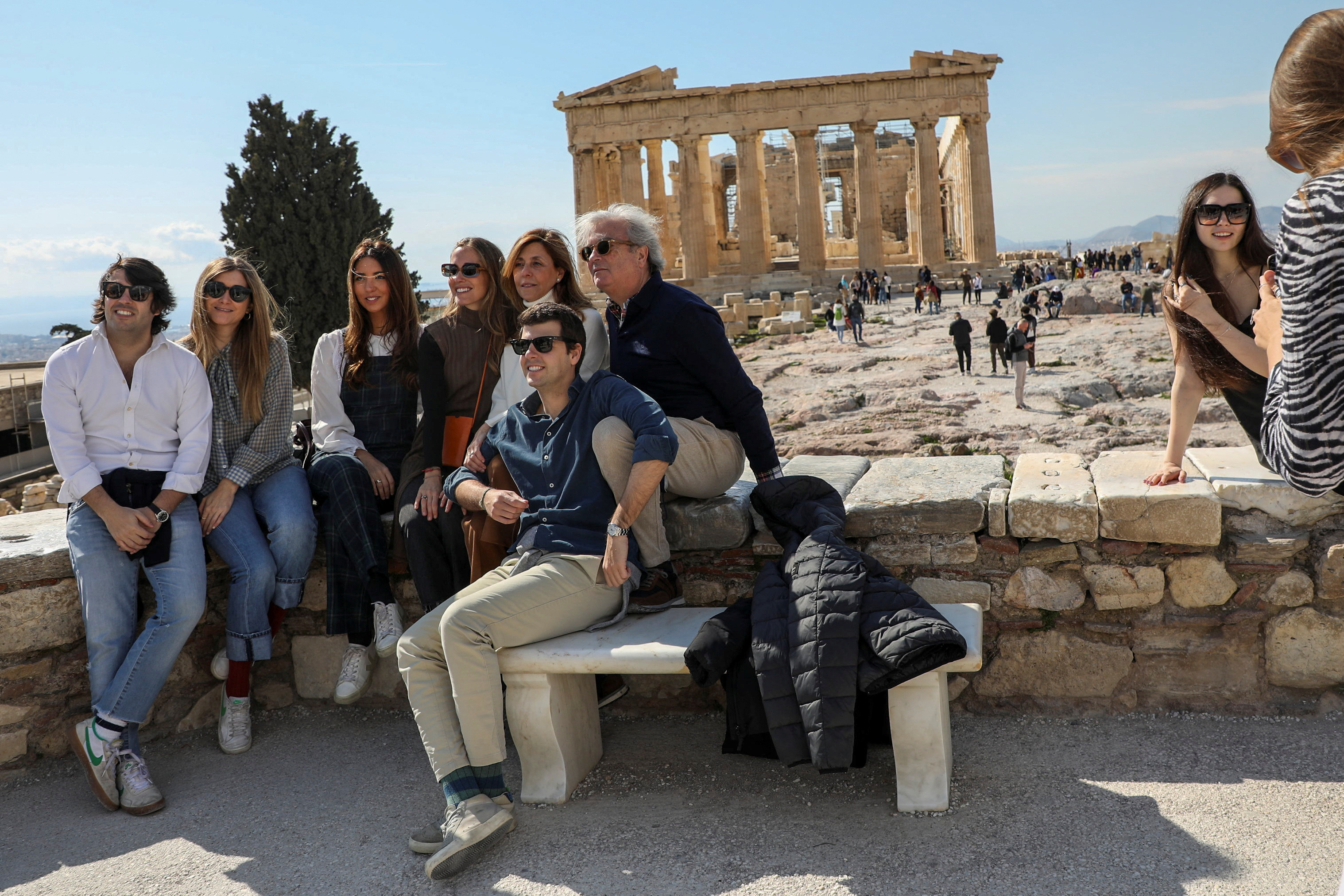 Visitors pose for a photo with the ancient Parthenon Temple seen in the background, atop the Acropolis hill archaeological site in Athens