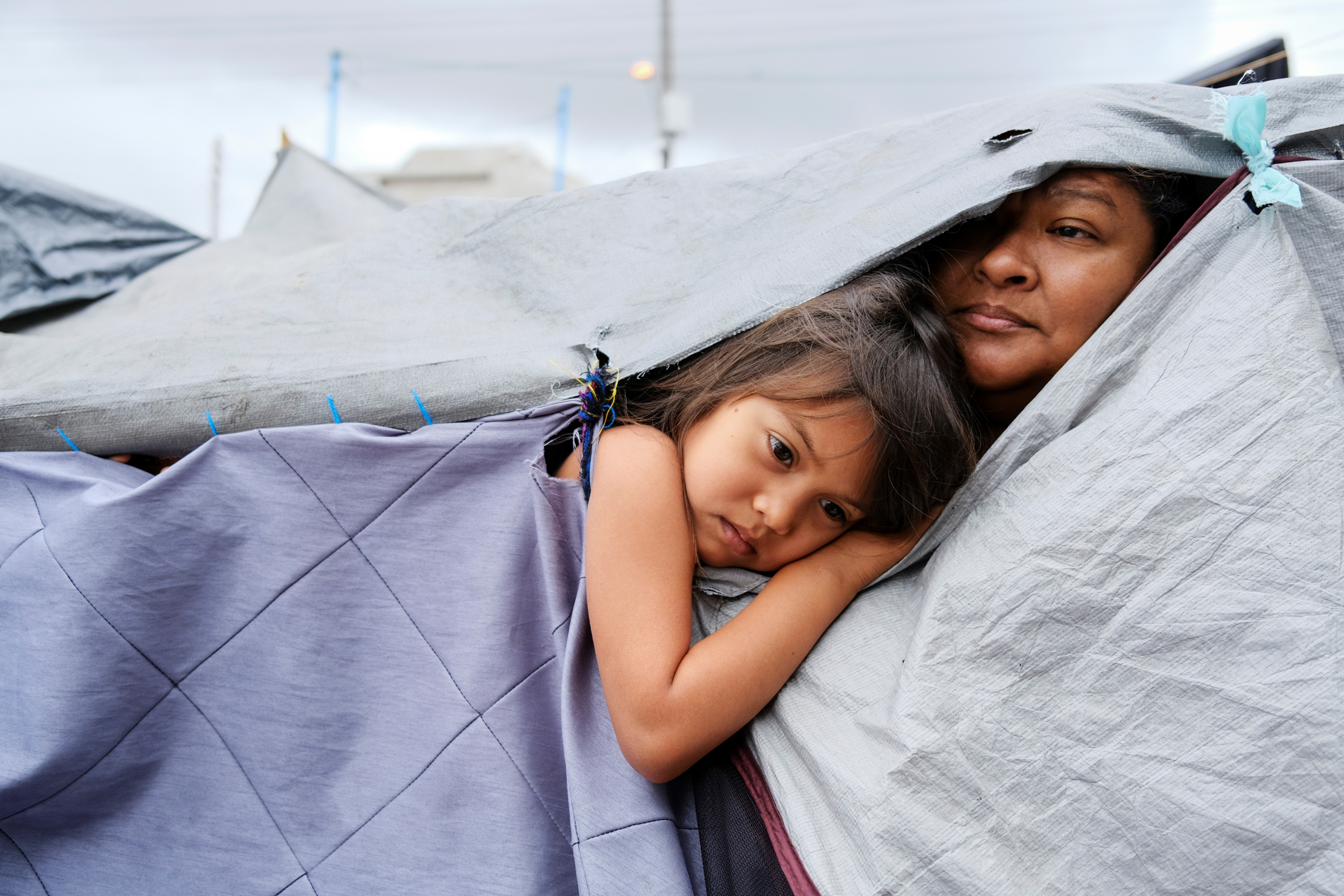 Honduran migrants Kami, 5, and her aunt Mariana listen as other migrants discuss hygiene norms within the migrant camp, at a makeshift camp at the El Chaparral border port of entry with the U.S., in Tijuana, Mexico April 22, 2021. Picture taken April 22, 2021. REUTERS/Toya Sarno Jordan