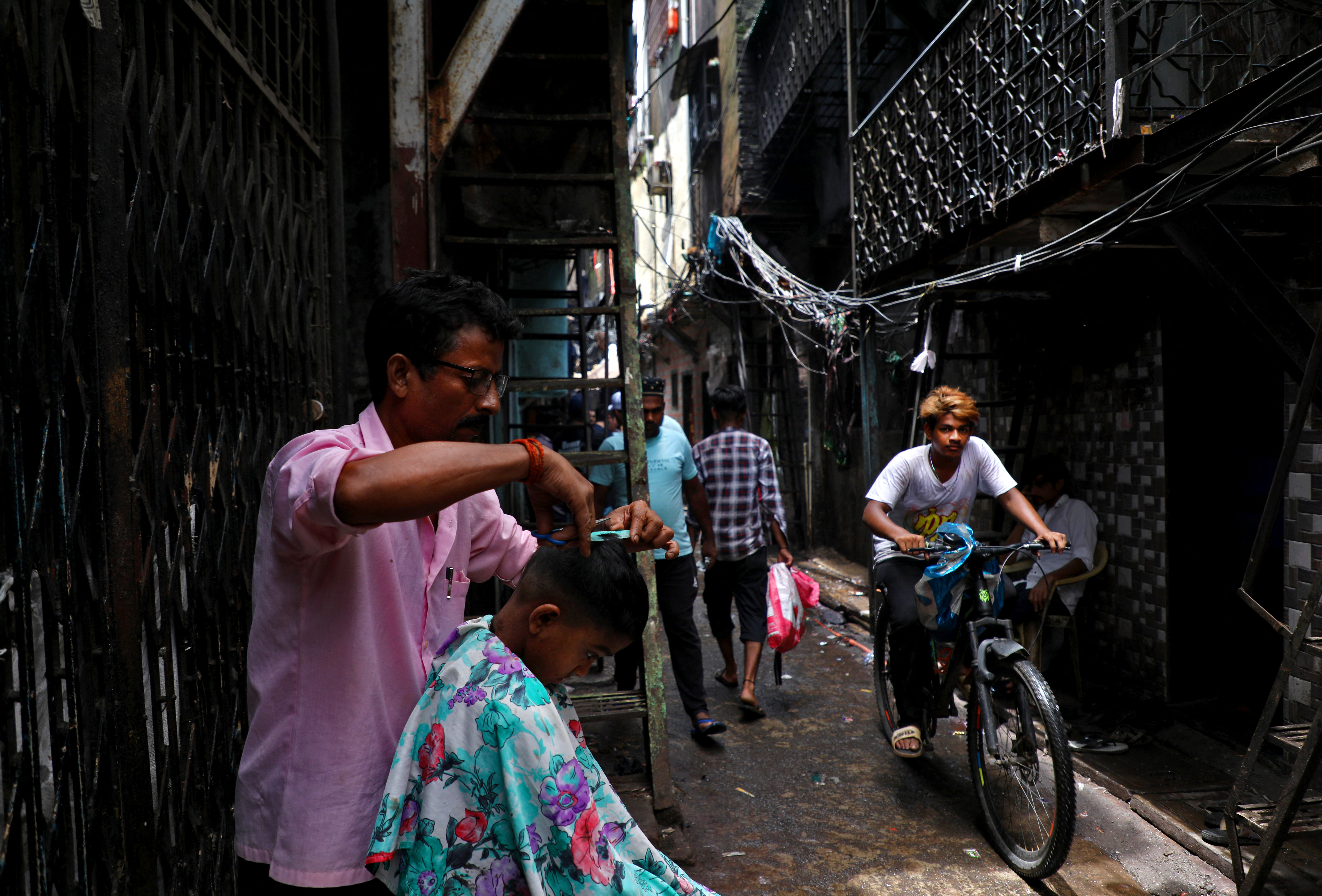 A boy gets a haircut from a barber in an alley in Dharavi, Mumbai