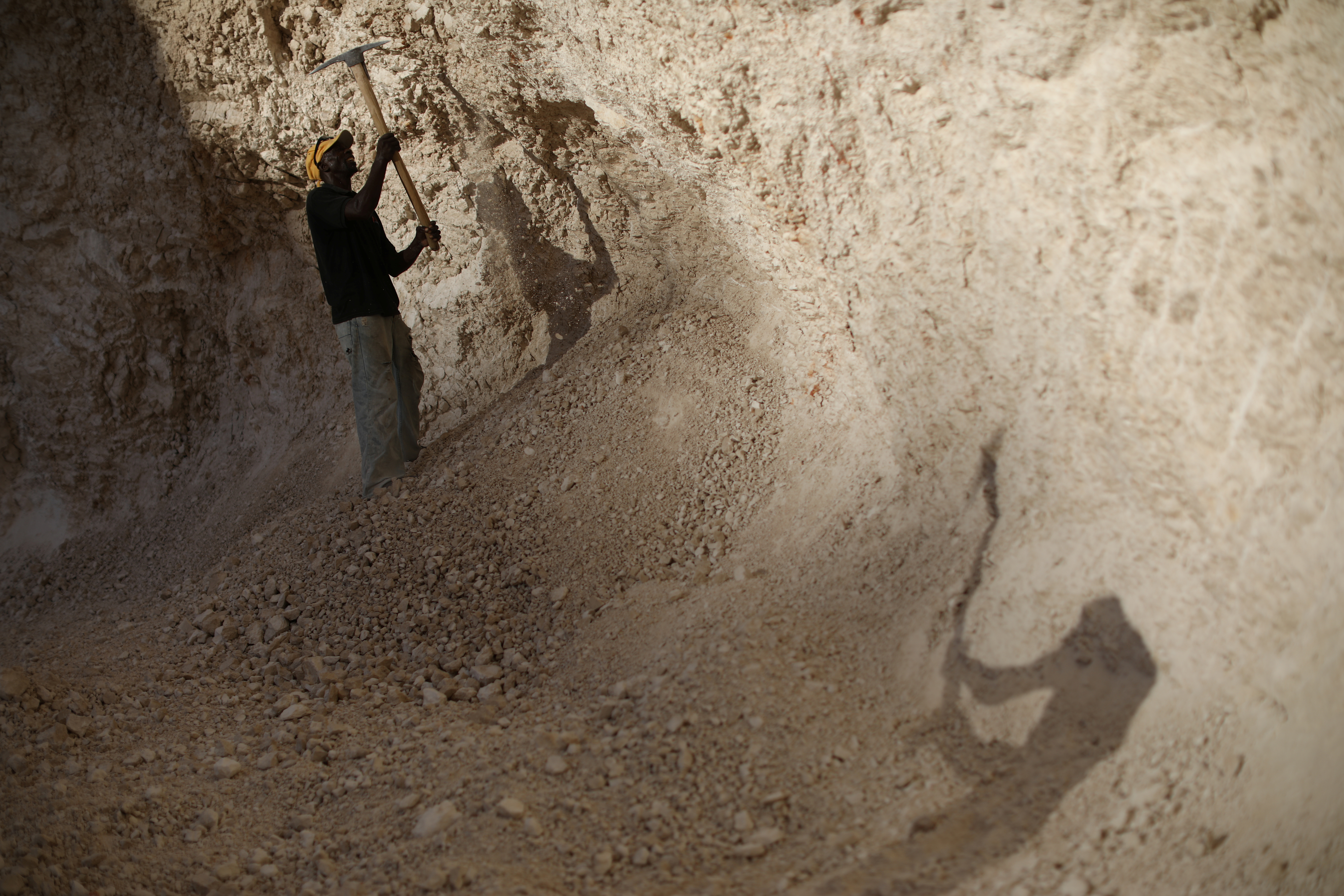 Men use picks to break rocks and get sand in a sand mine on the outskirts of Fond Parisien