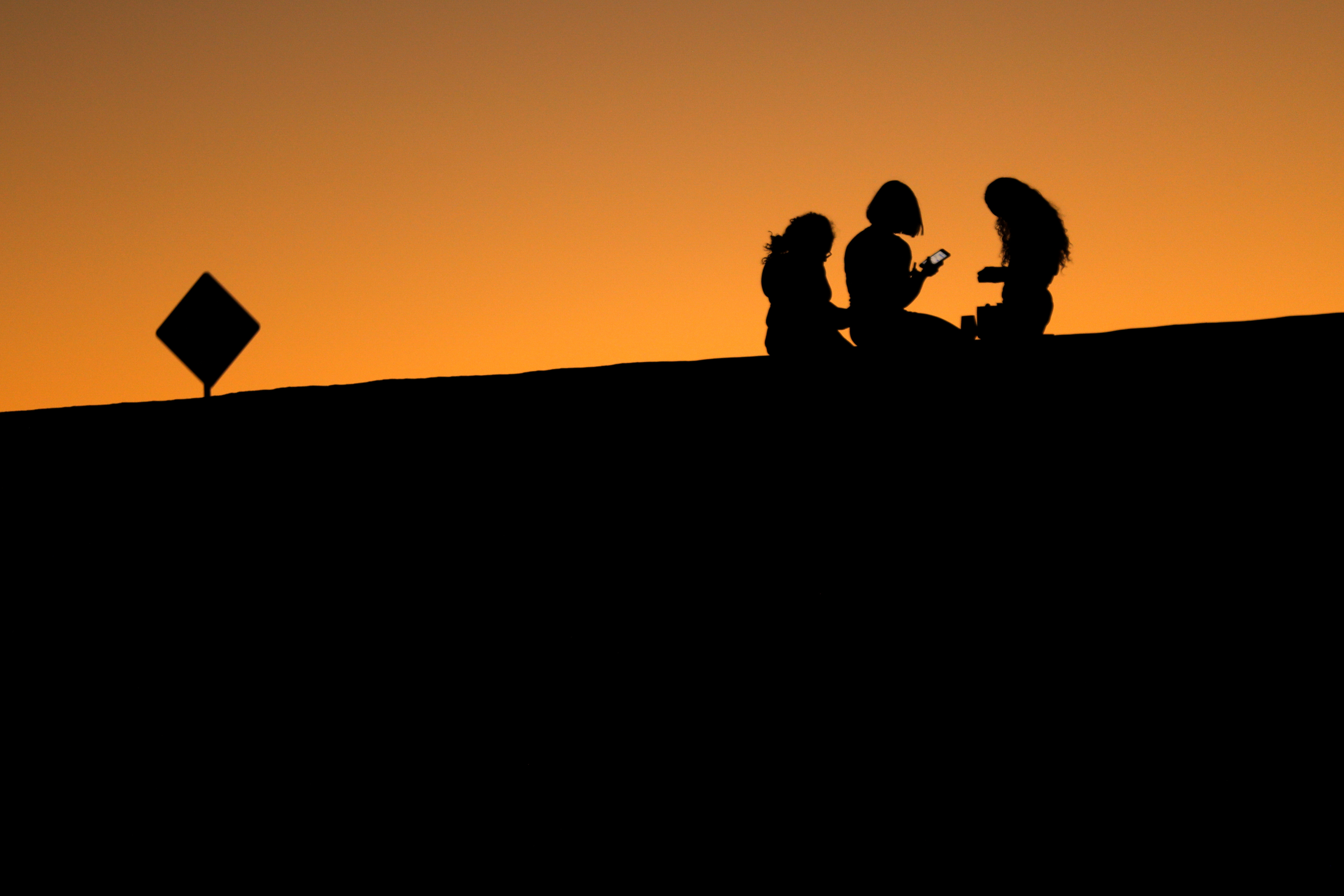 Young girls look at their phones as they sit on a hillside after sun set in El Paso, Texas