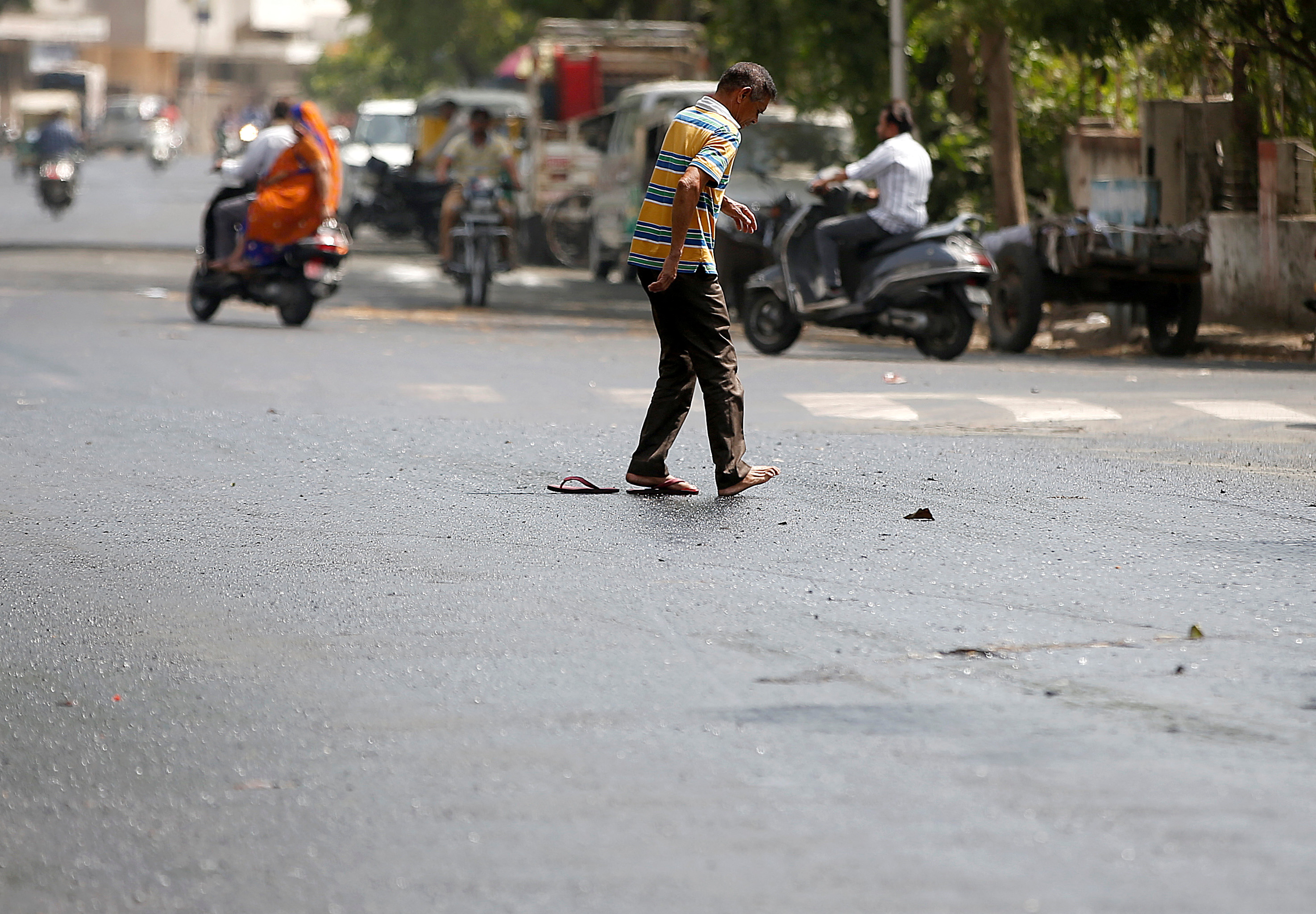 A man struggles to cross a road after his slippers got stuck in melted tar on a hot weather day in Ahmedabad