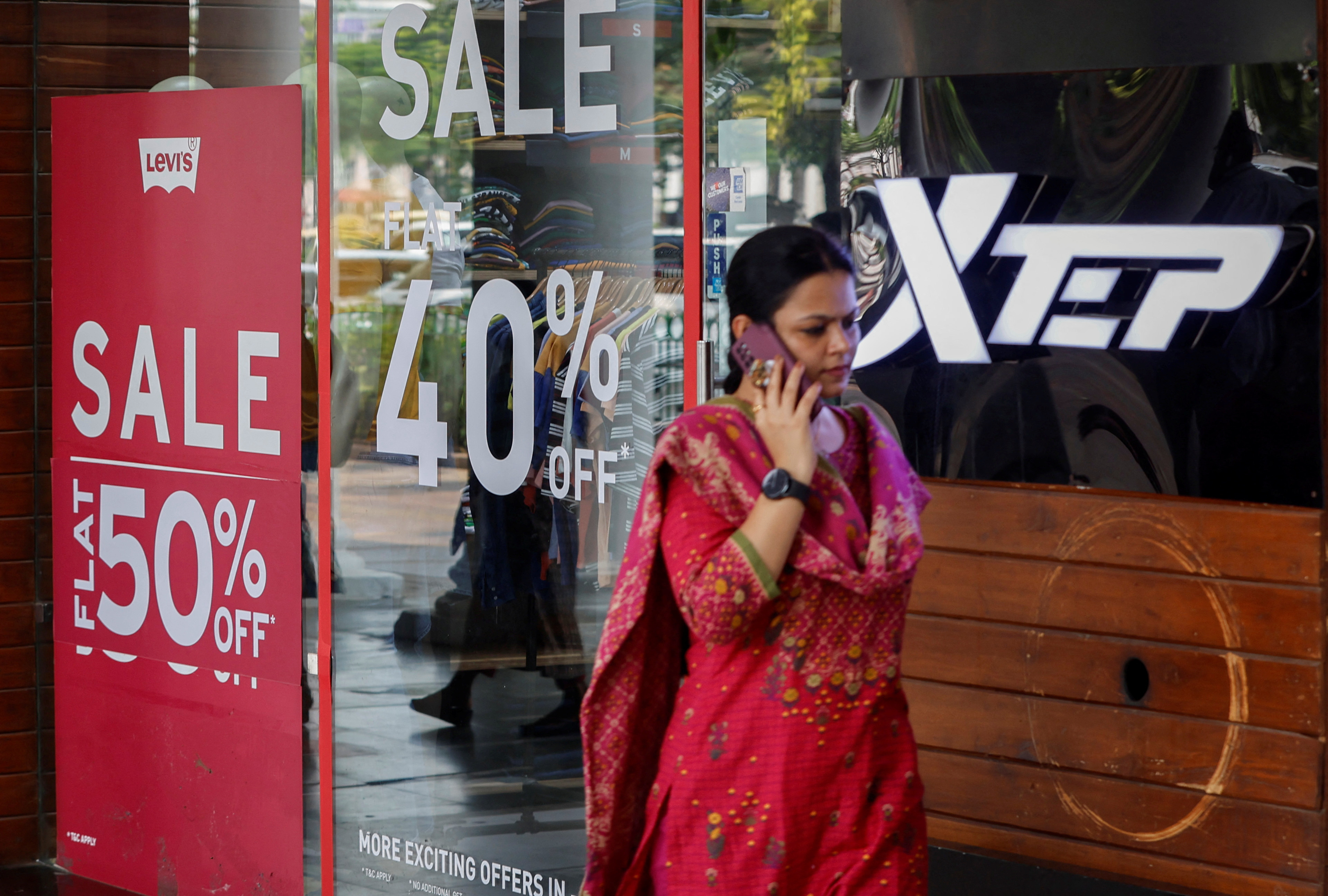 Woman walks past a retail store with signs advertising a sale in New Delhi