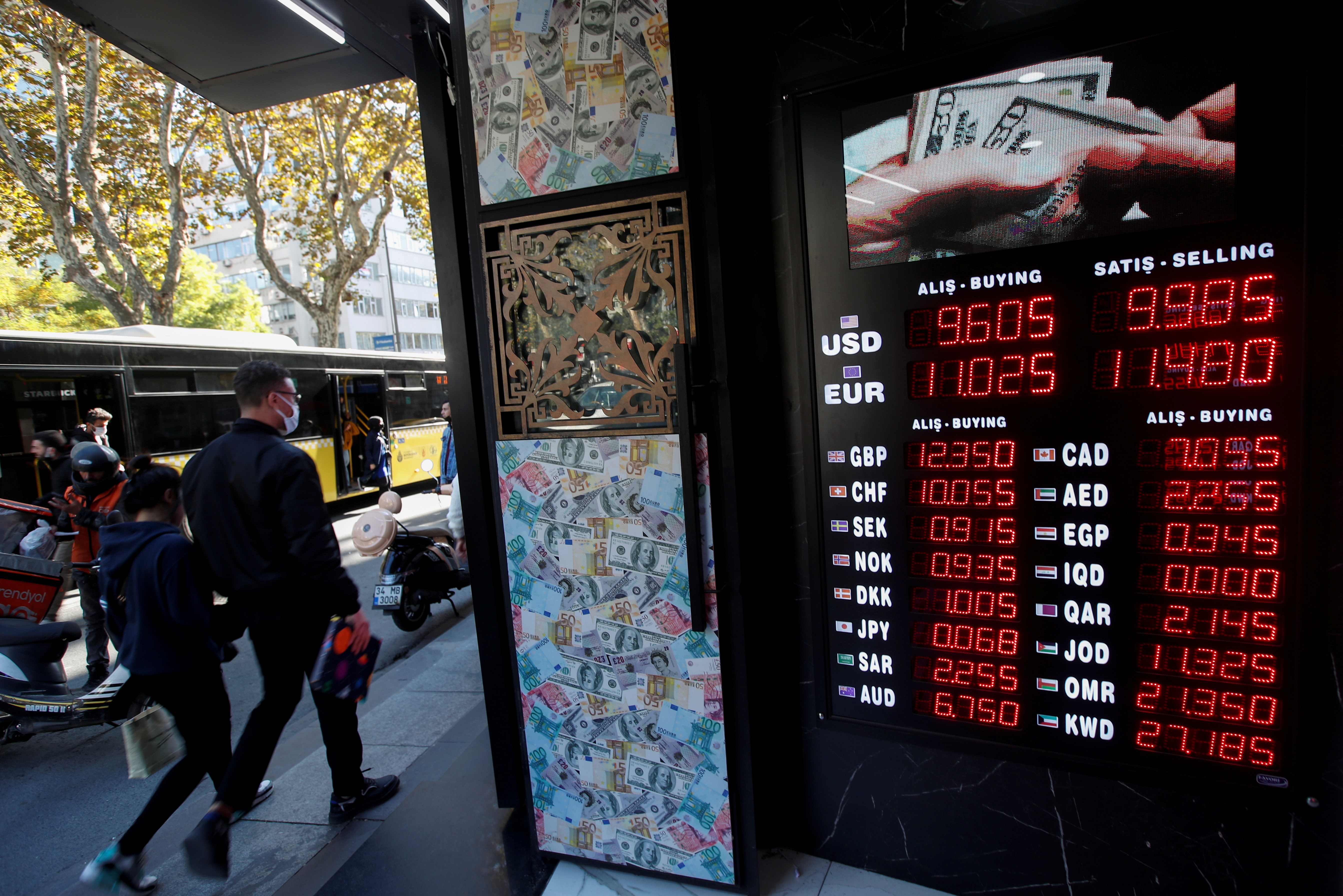 People walk past a board showing the currency exchange rates outside an exchange office in Istanbul