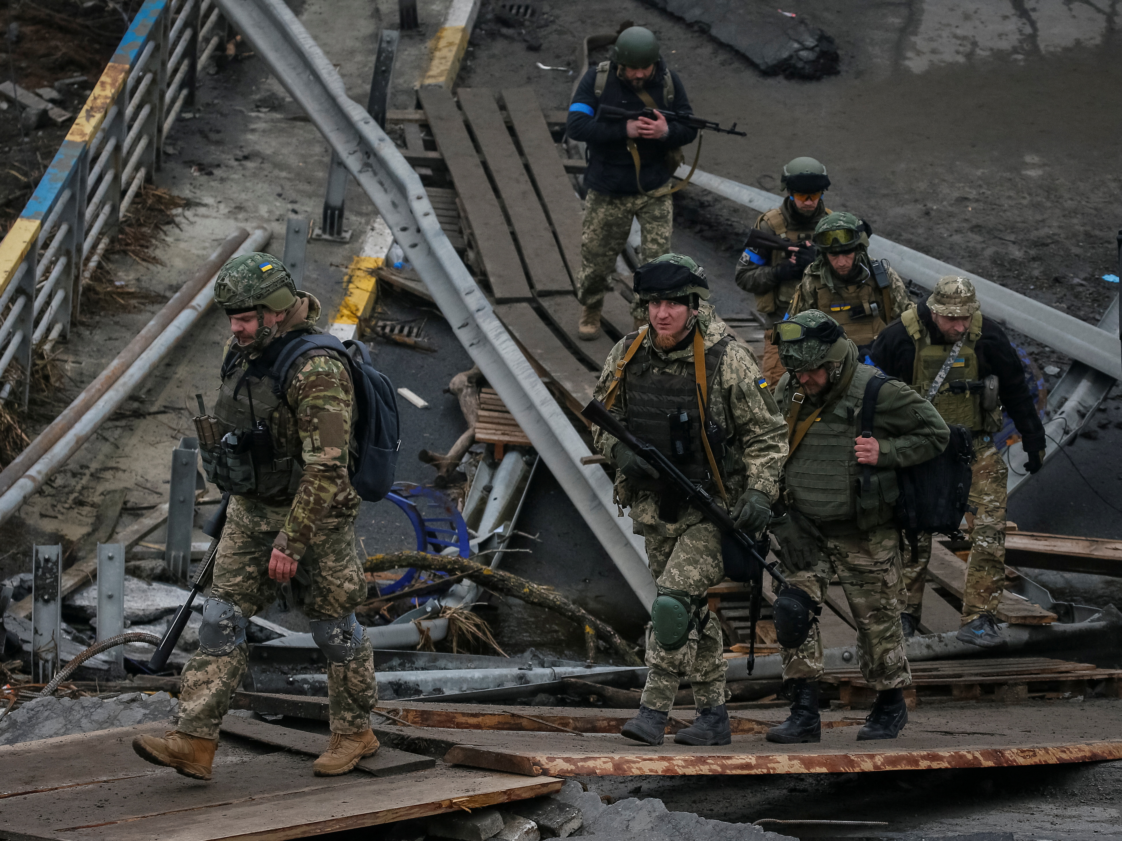 Ukrainian servicemen walk on a destroyed bridge in the town of Irpin