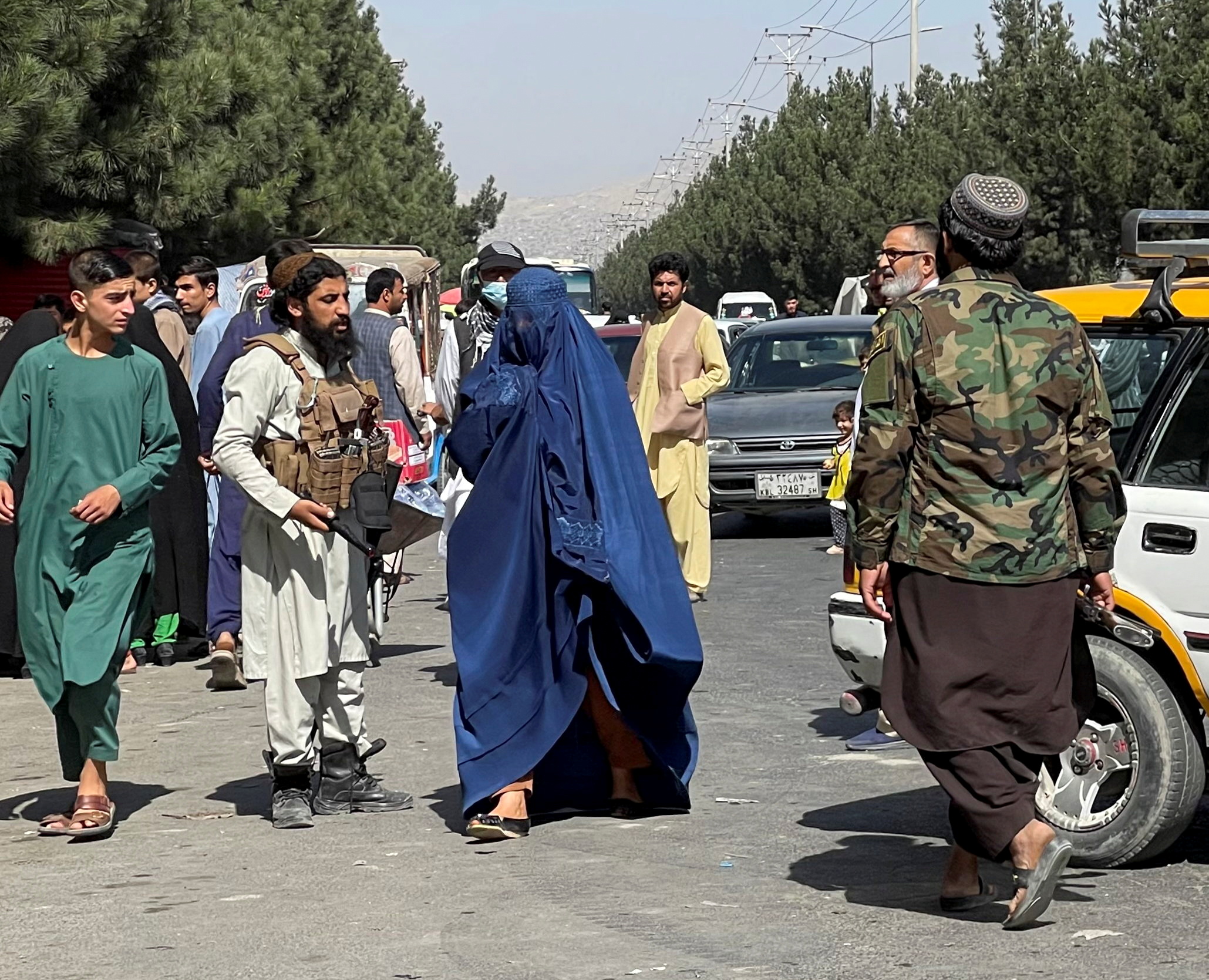 Taliban forces block the roads around the airport, while a woman with Burqa walks passes by, in Kabul