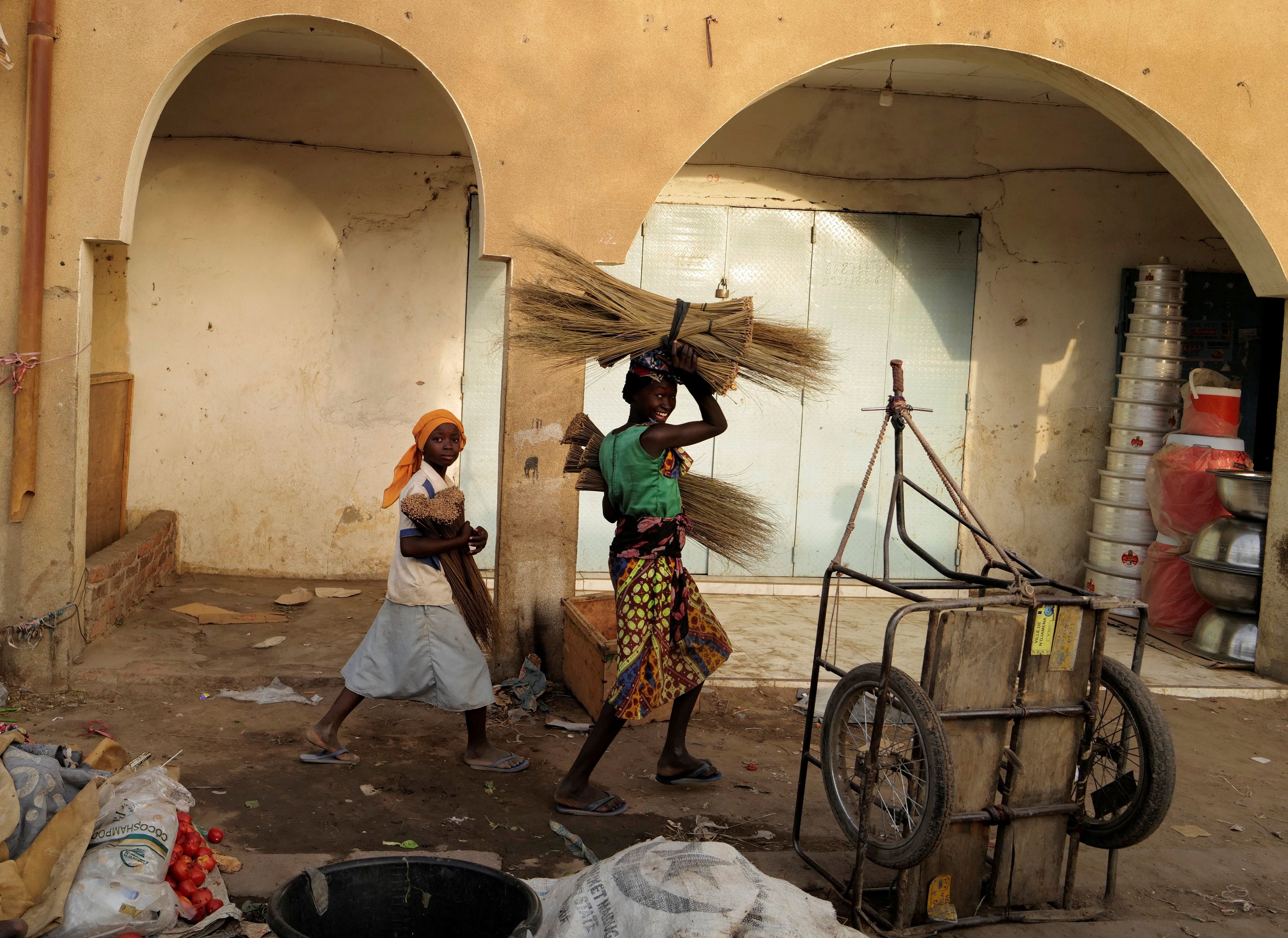 Street vendor girls carry brooms for sale at the market in N'djamena