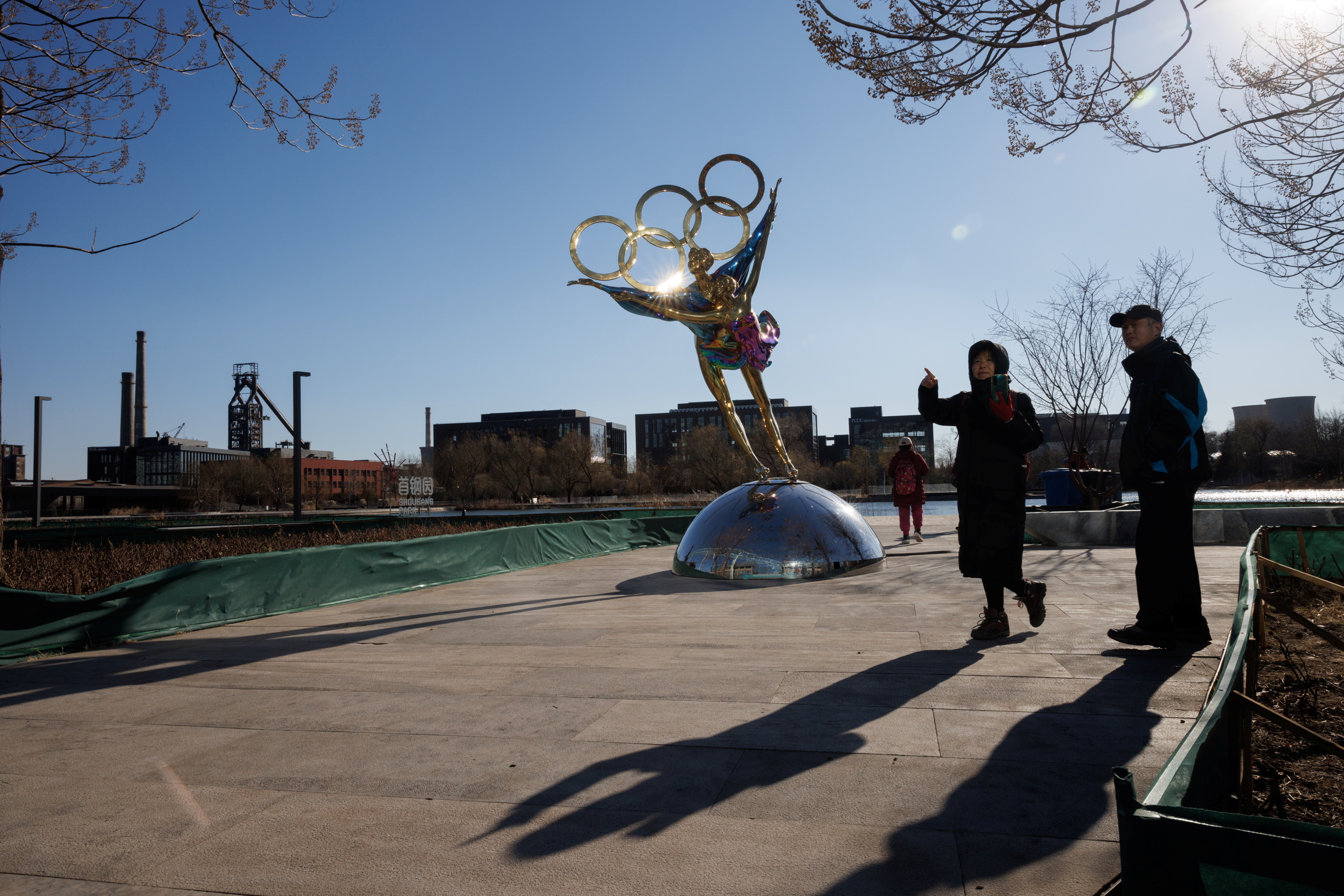 People stand next to a statue featuring the Olympic Rings outside the headquarters of the Beijing Organising Committee for the 2022 Olympic and Paralympic Winter Games in Shougang Park, the site of a a former steel mill, in Beijing, China, November 30, 2021.  REUTERS/Thomas Peter