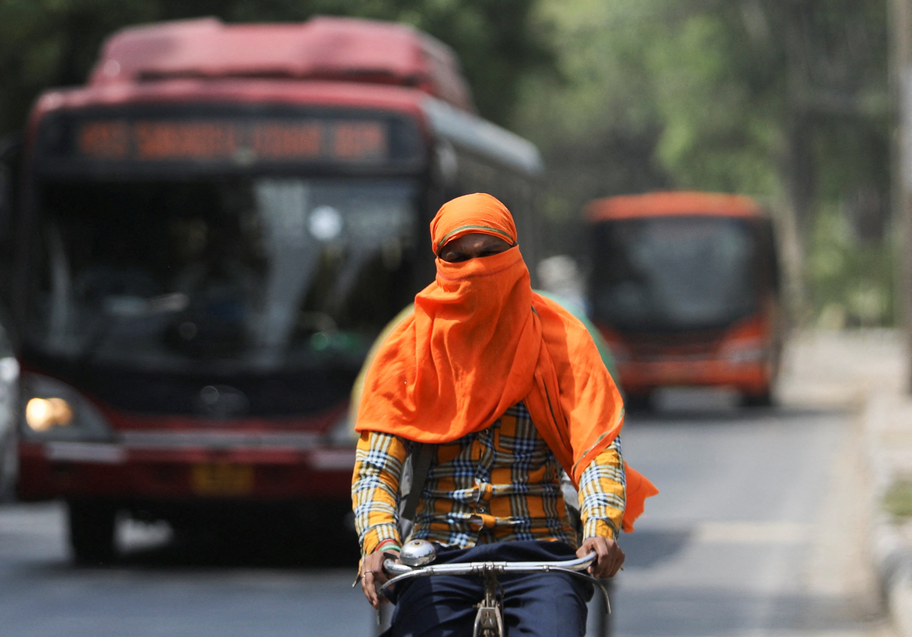 A man rides a cycle with his face fully covered on a hot summer day, in New Delhi