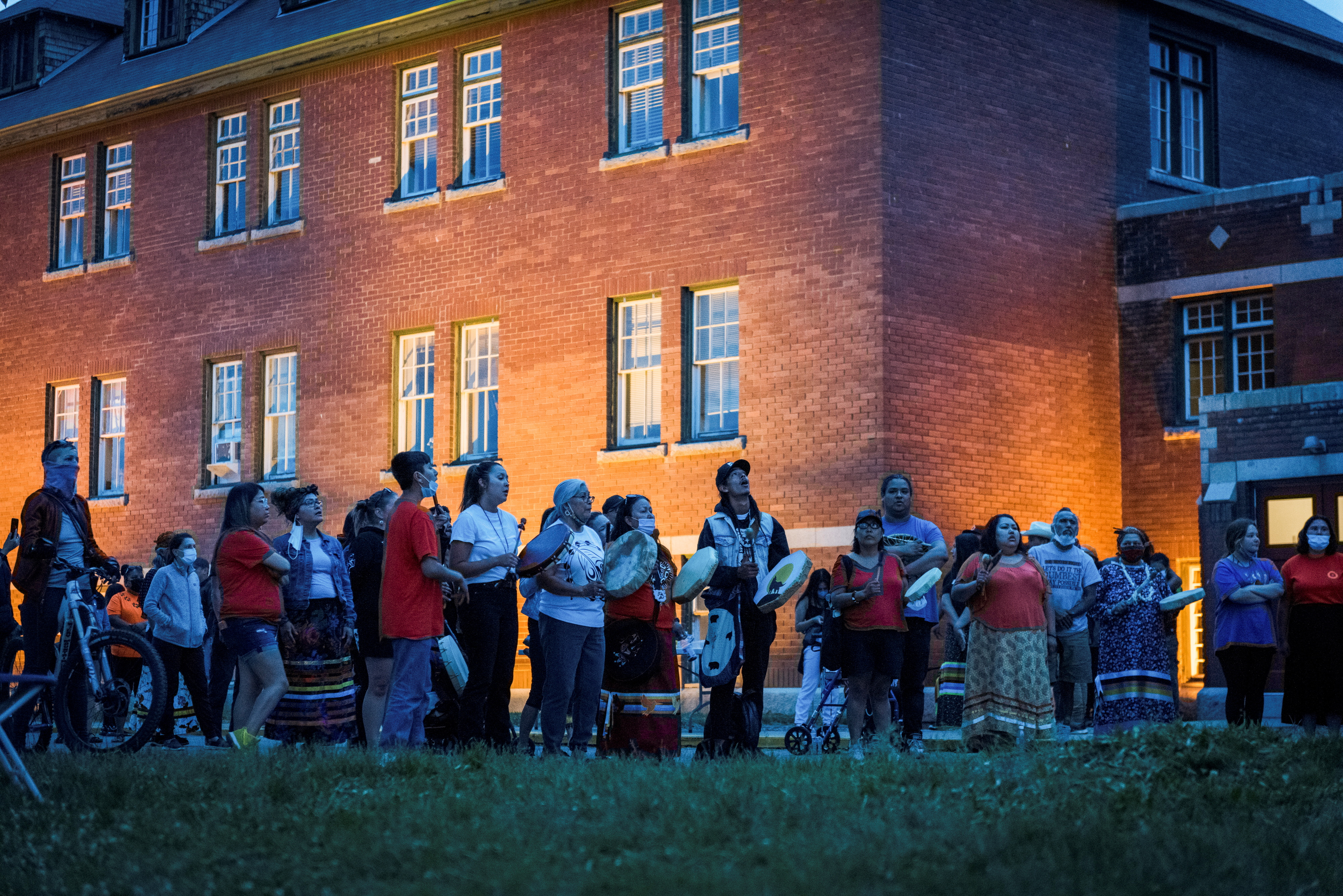 People gather to listen to drummers and singers at a memorial in front of the former Kamloops Indian Residential School
