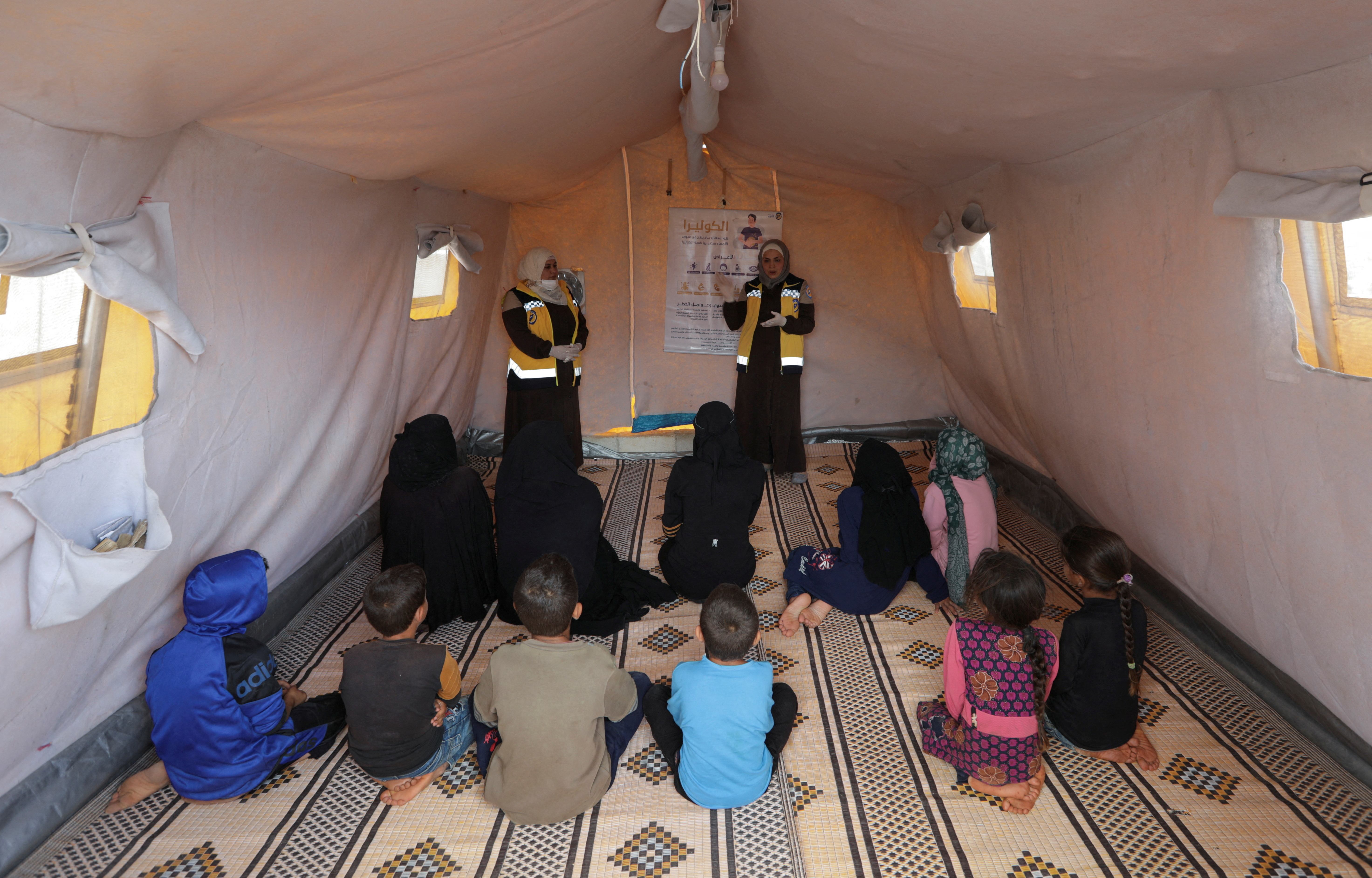 Civil defense members talk to internally displaced Syrians during a cholera awareness campaign, at a camp in northern rebel-held Idlib