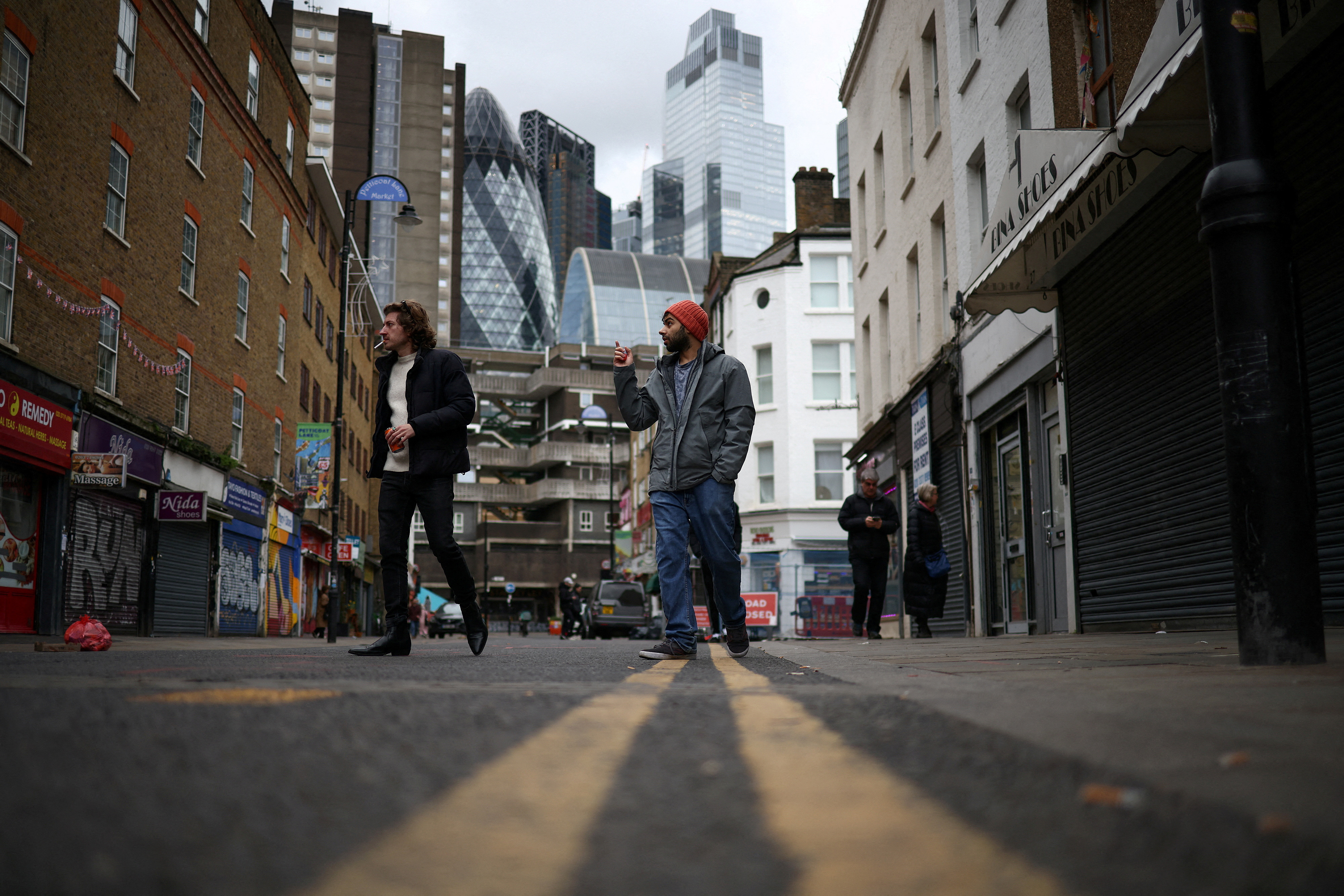 People walk past shops, with the City of London financial district in the background, in London, Britain