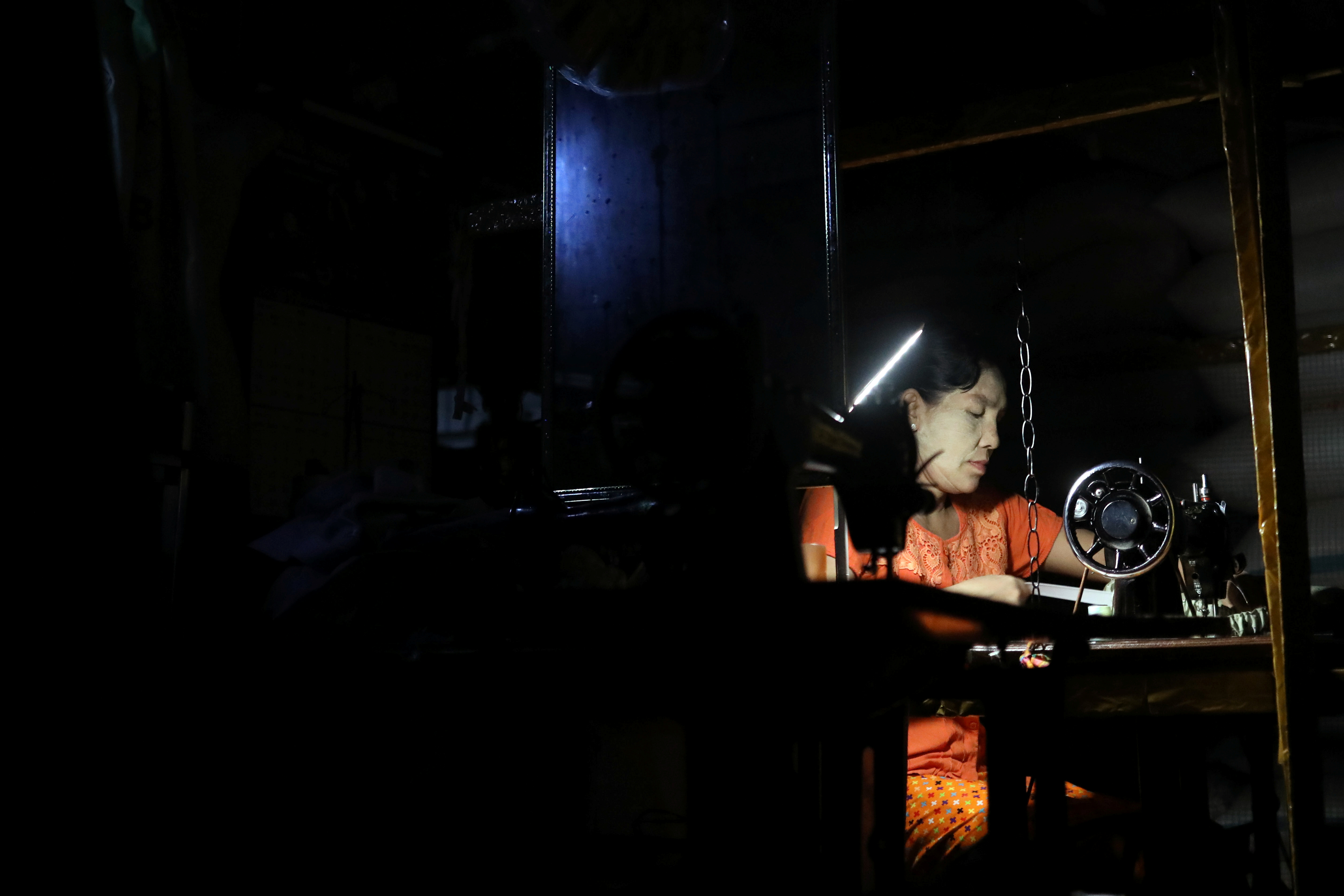 A woman works on her sewing machine with mobile lighting during a power outage in Yangon