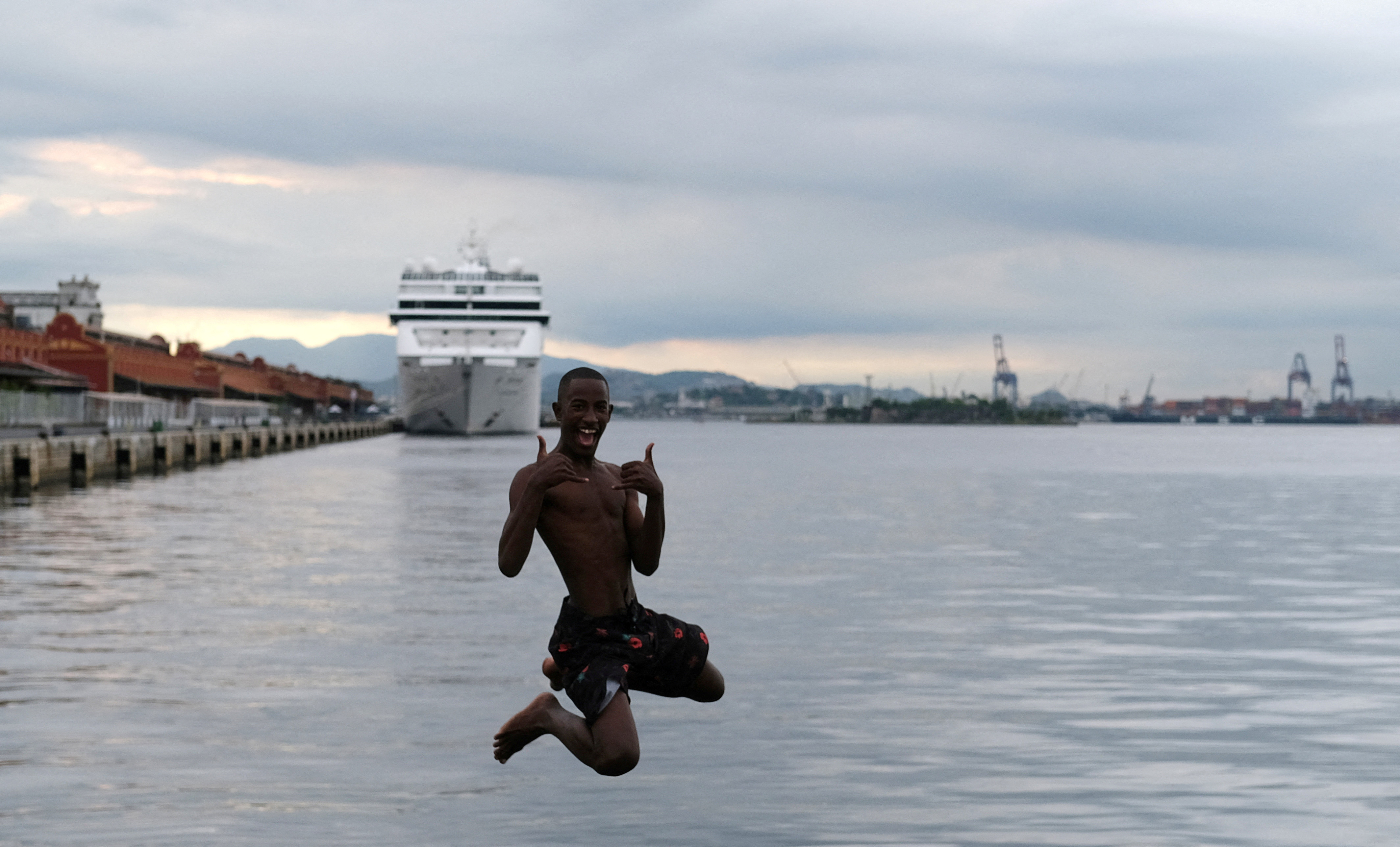 A youth jumps into the waters of Guanabara Bay, next to a cruise ship docked at Rio de Janeiro port