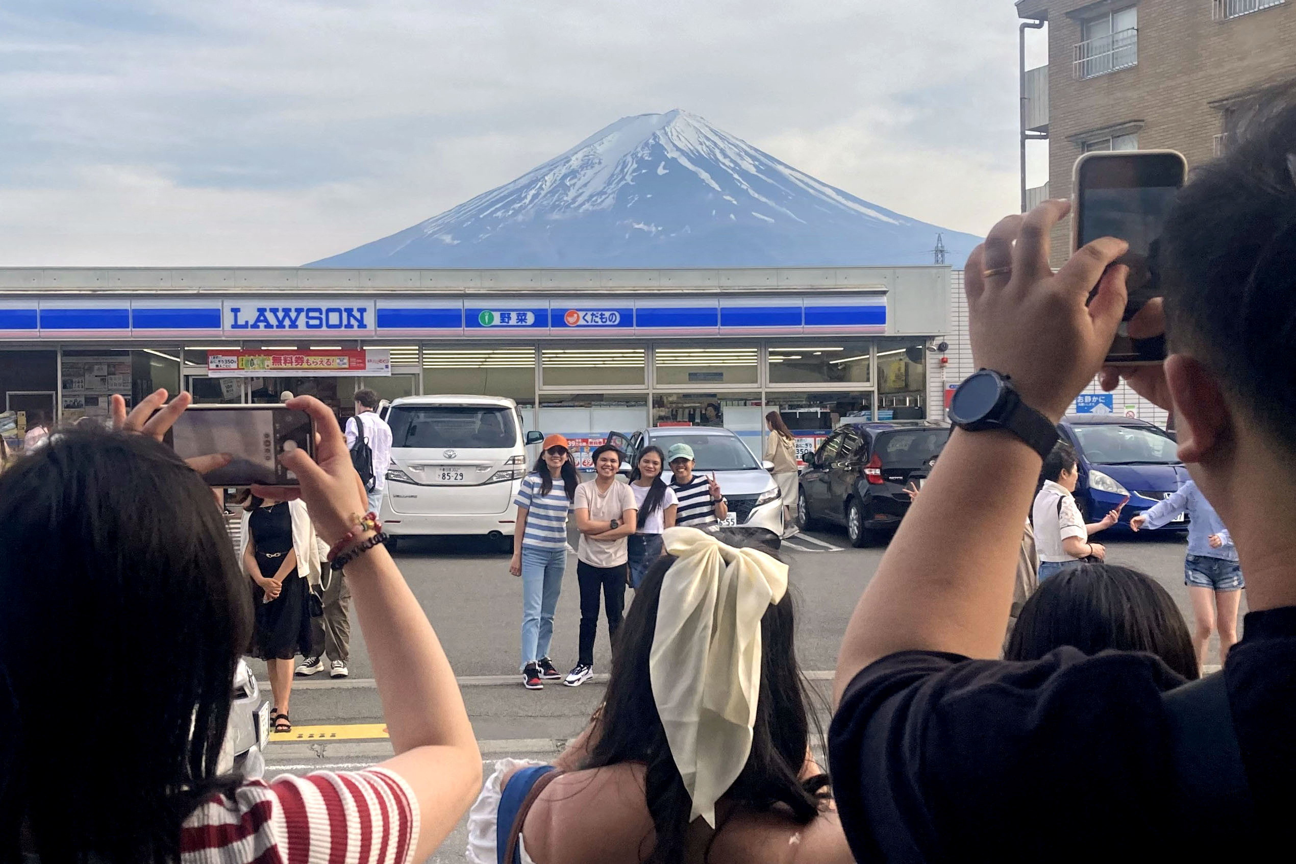 Tourists take photos of Mount Fuji appearing over a convenience store in Fujikawaguchiko town