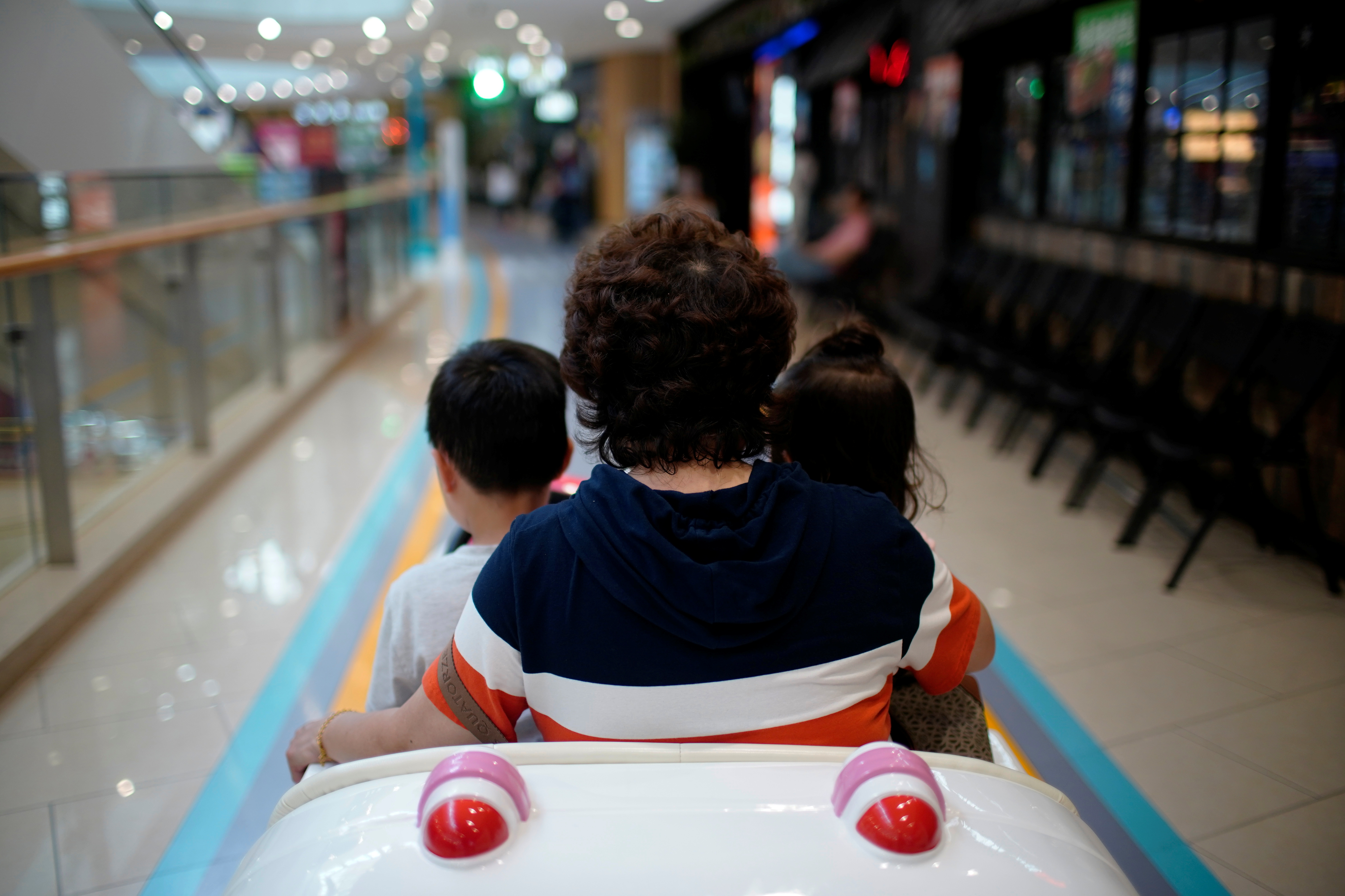 Person sits in a toy car with children at a shopping mall in Shanghai