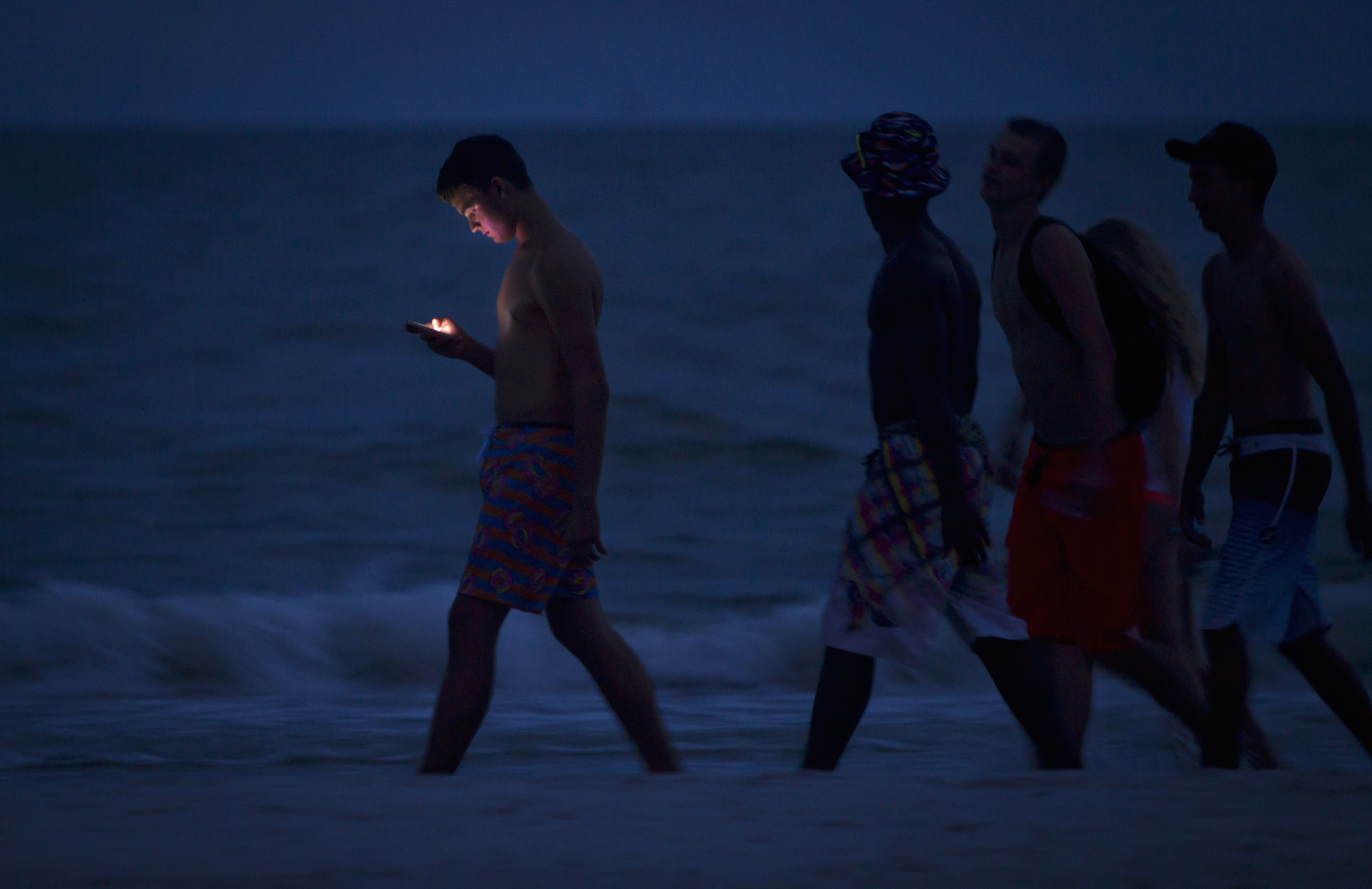 File photo of a person looksing at cell phone as he and others walk along beach at twilight during Labour Day long weekend in Ft Myers Beach, Florida