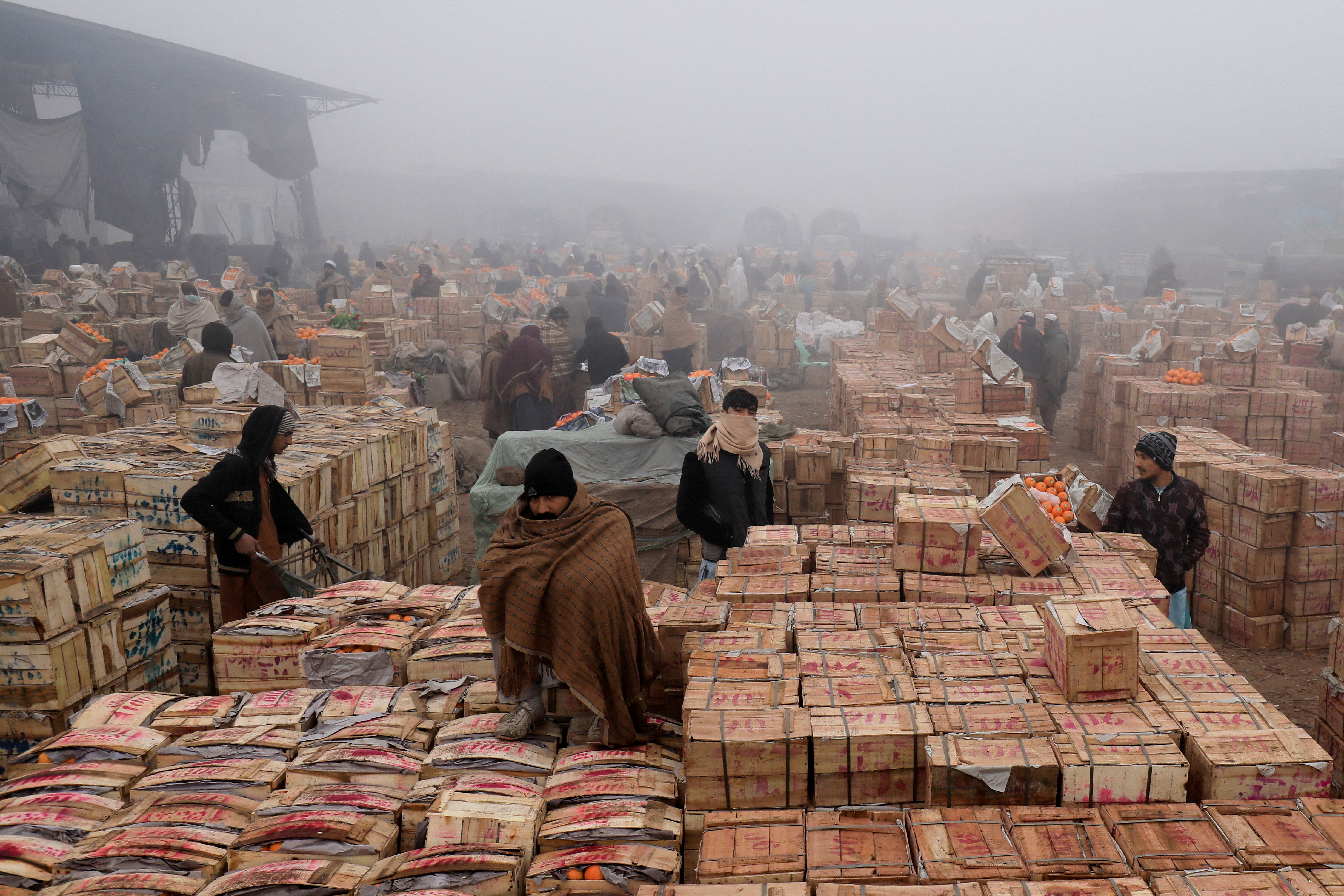 People cover themselves to stay warm during heavy fog, early in the morning at the fruit wholesale market on the outskirts of Peshawarr