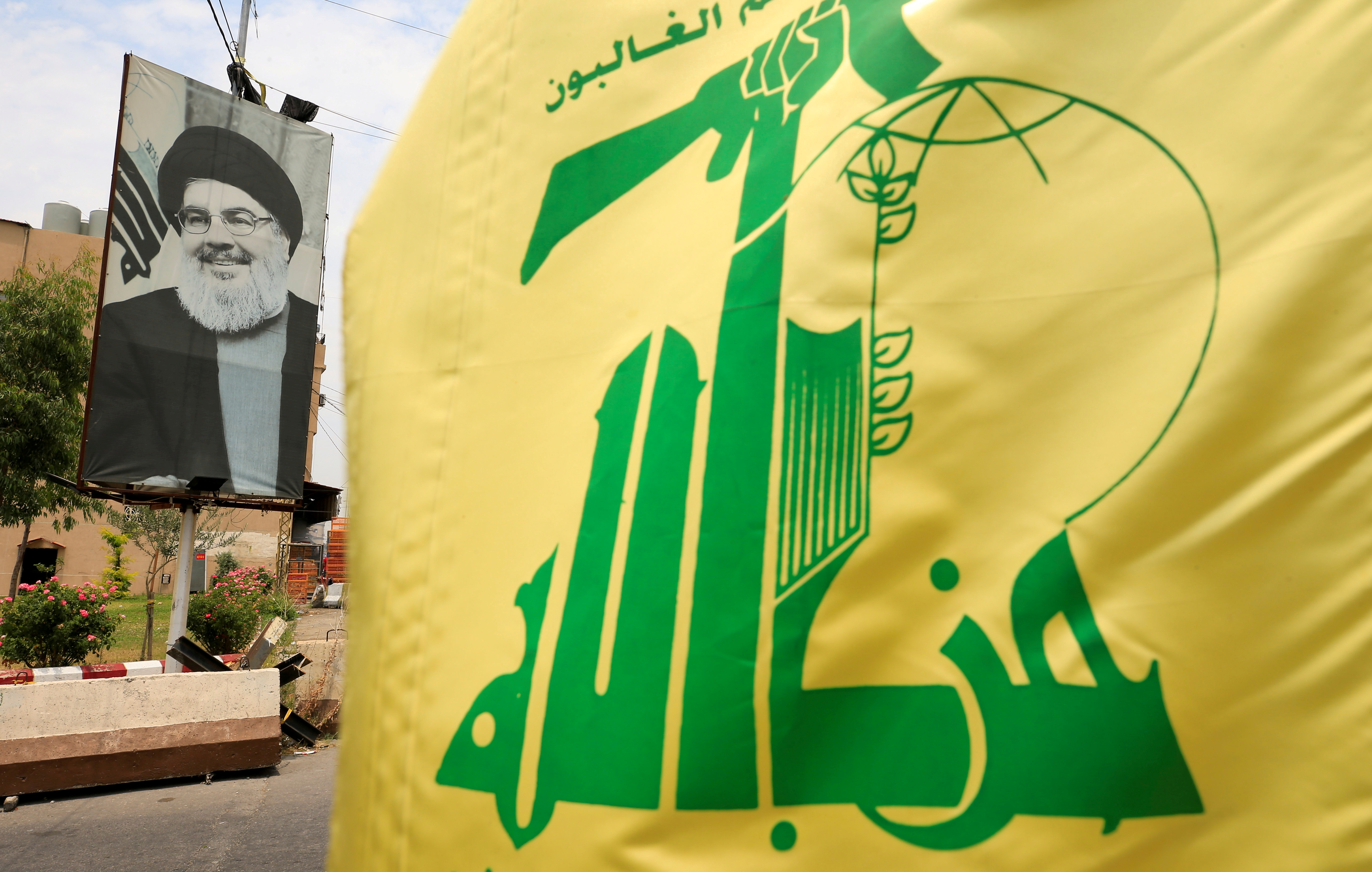 A Hezbollah flag and a poster depicting Lebanon's Hezbollah leader Sayyed Hassan Nasrallah are pictured along a street, near Sidon