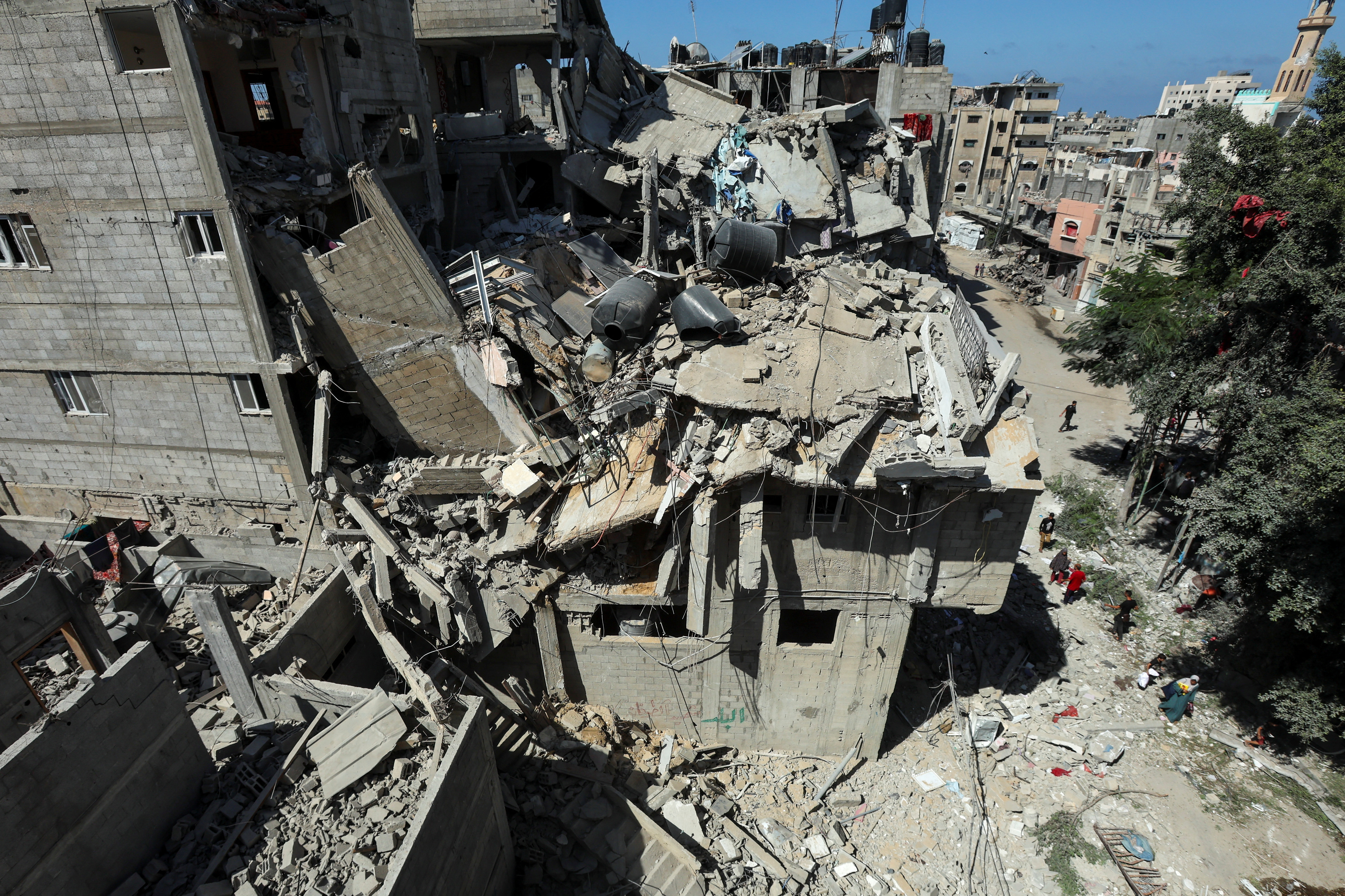 Palestinians walk past a house hit in an Israeli strike, amid the Israel-Hamas conflict, in Bureij refugee camp, in the central Gaza Strip