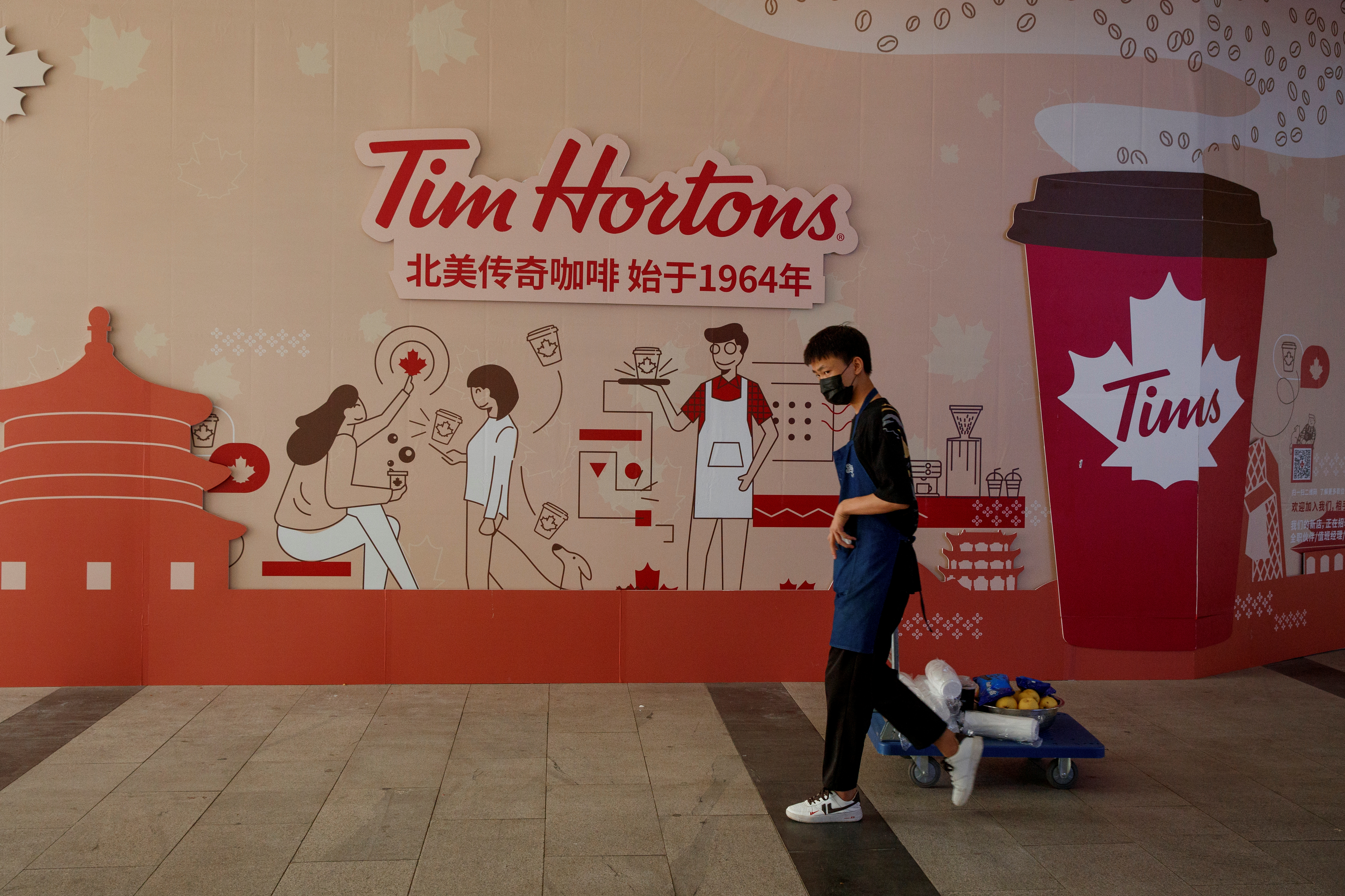 A man walks past a store front poster advertising the opening of a cafe of the Canadian coffee and fastfood chain Tim Hortons in Beijing