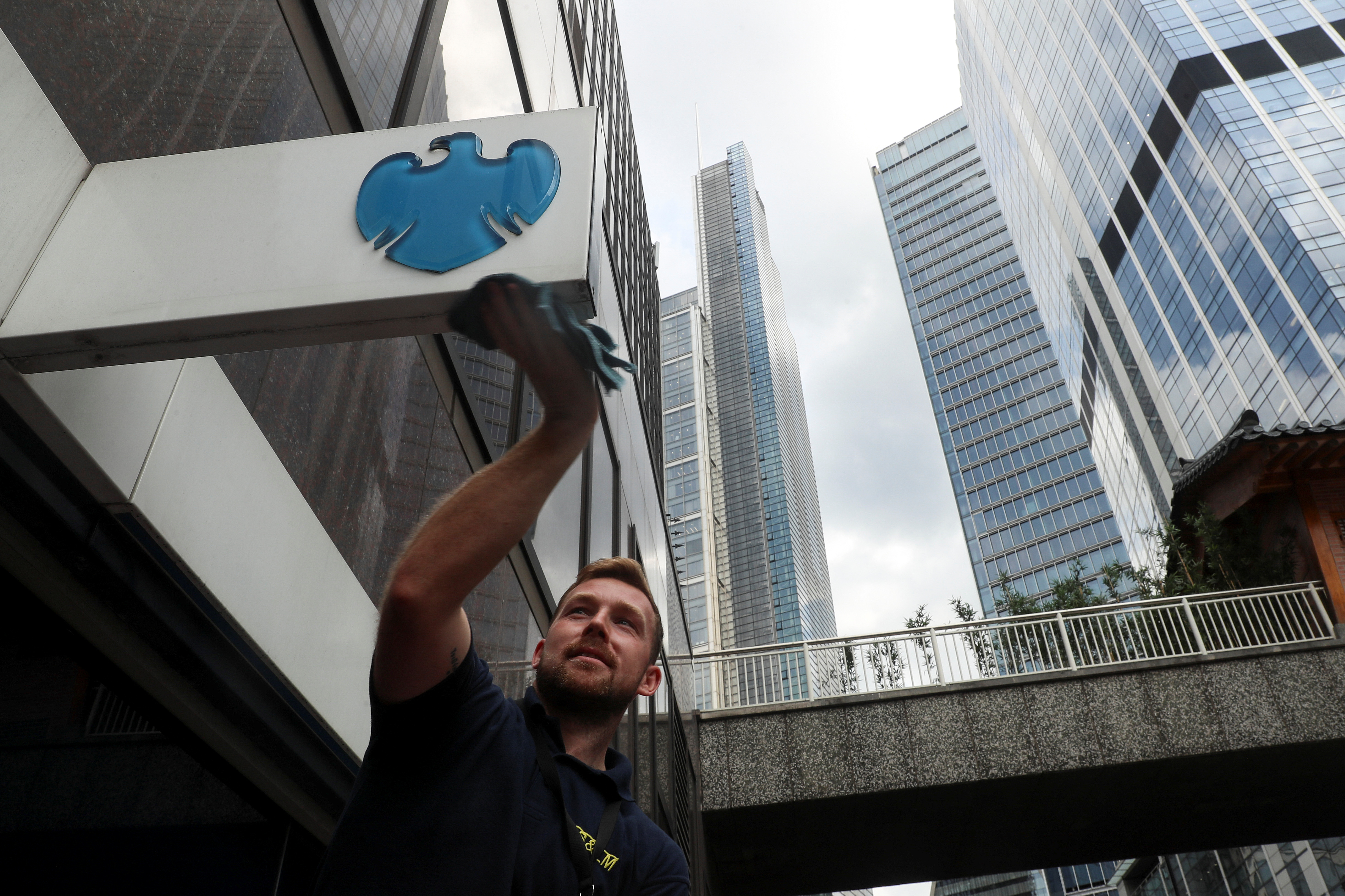 A worker cleans a Barclays logo outside a bank branch in the financial district of London