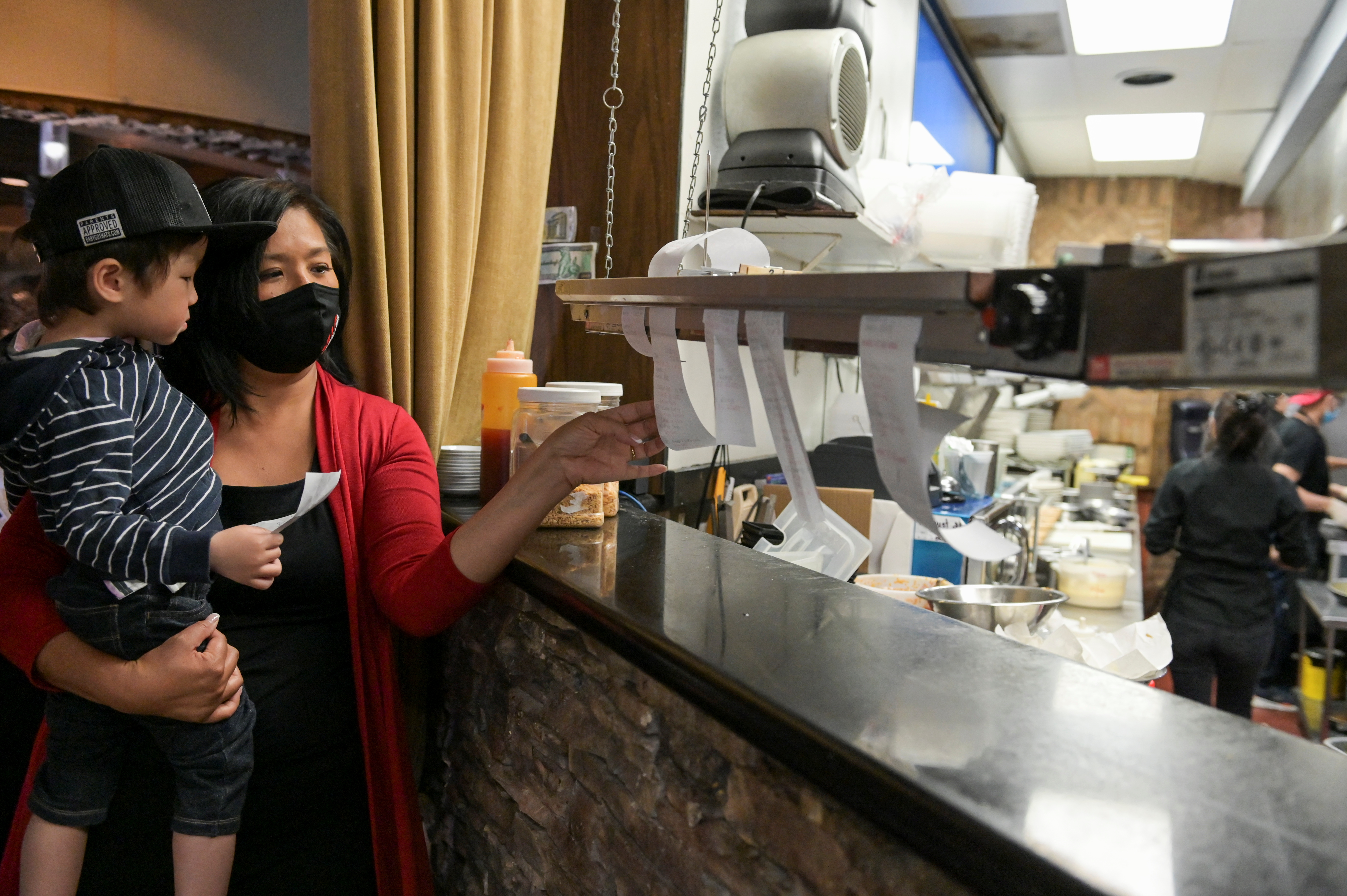 Owner Jan-le Low holds nephew Jackson Low as she moves order tickets at Satay Thai Bistro and Bar, amid the coronavirus disease (COVID-19) outbreak, in Las Vegas, Nevada, U.S., March 28, 2021. REUTERS/Bridget Bennett