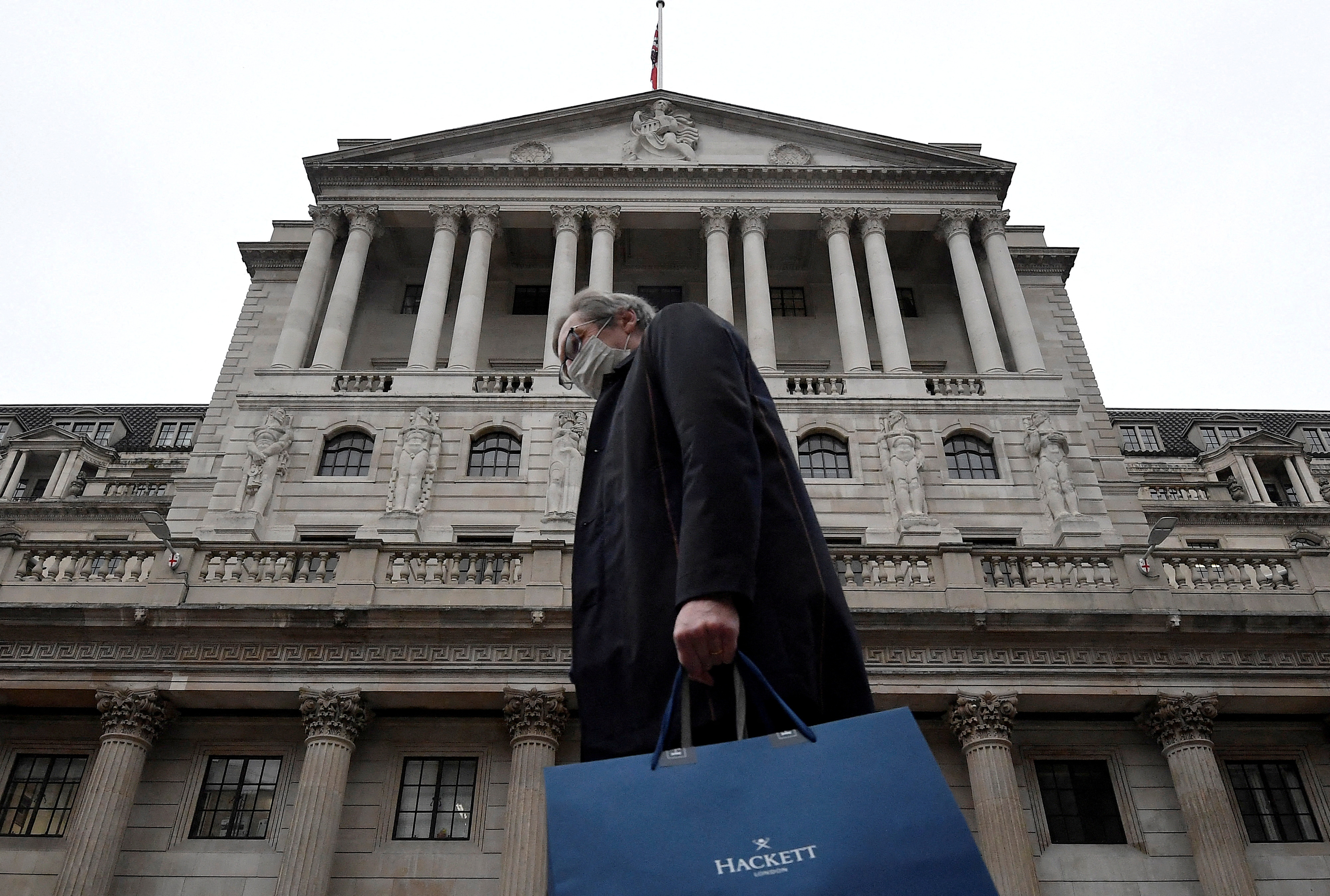 A man wearing a protective face mask walks past the Bank of England (BoE),