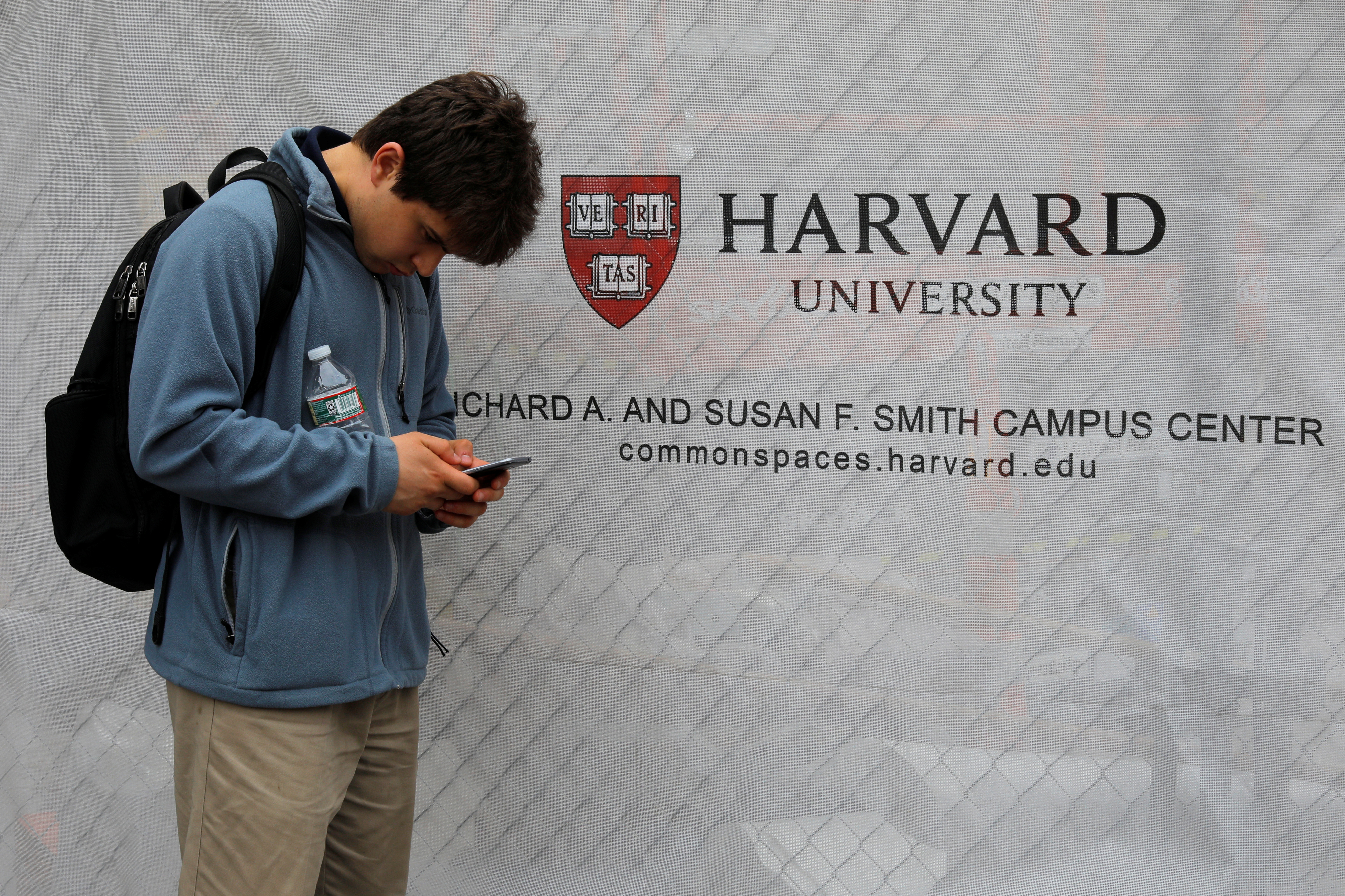 A man looks at his mobile phone beside a sign for Harvard University in Cambridge