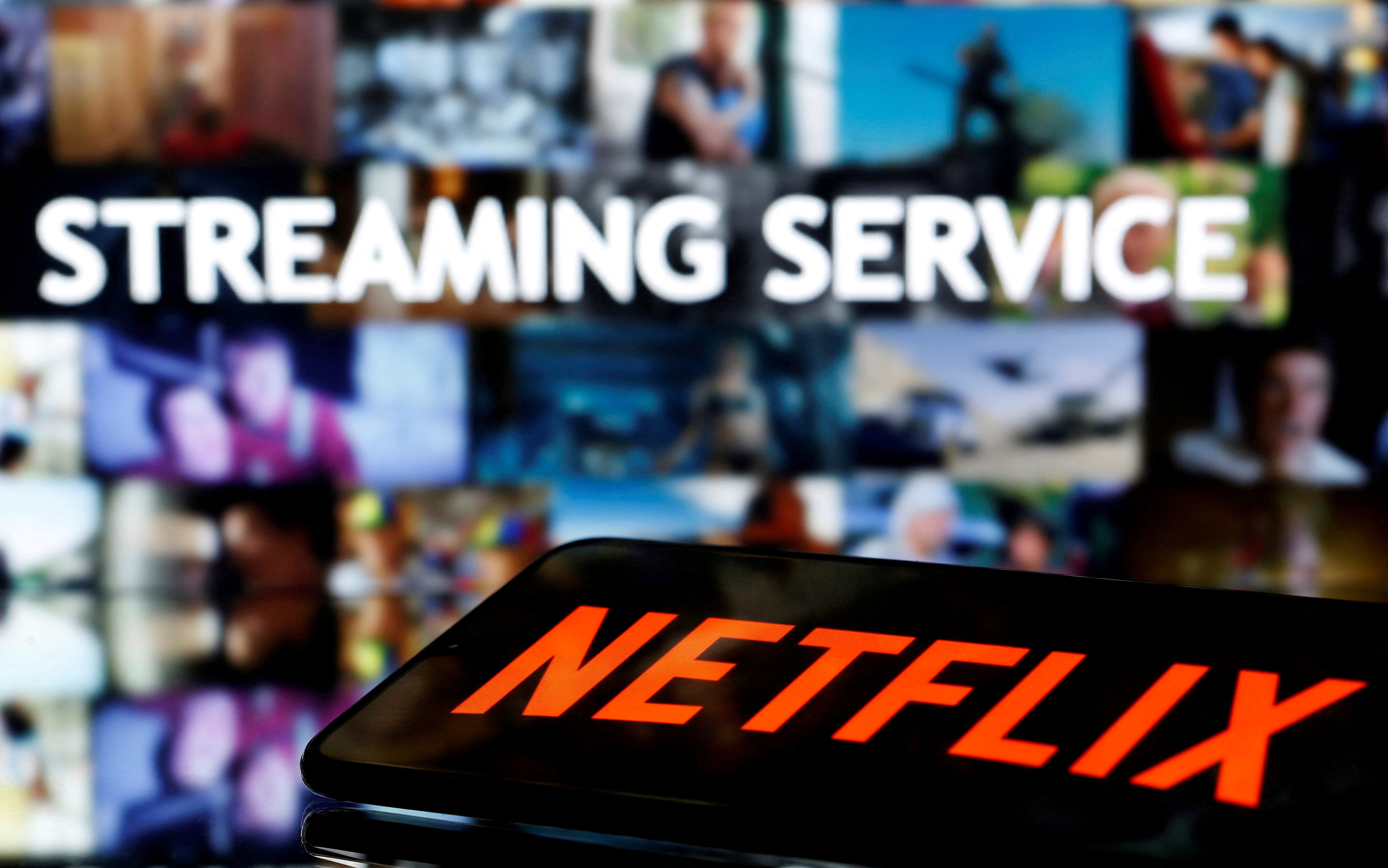 A smartphone with the Netflix logo lies in front of displayed "Streaming service" words in this illustration