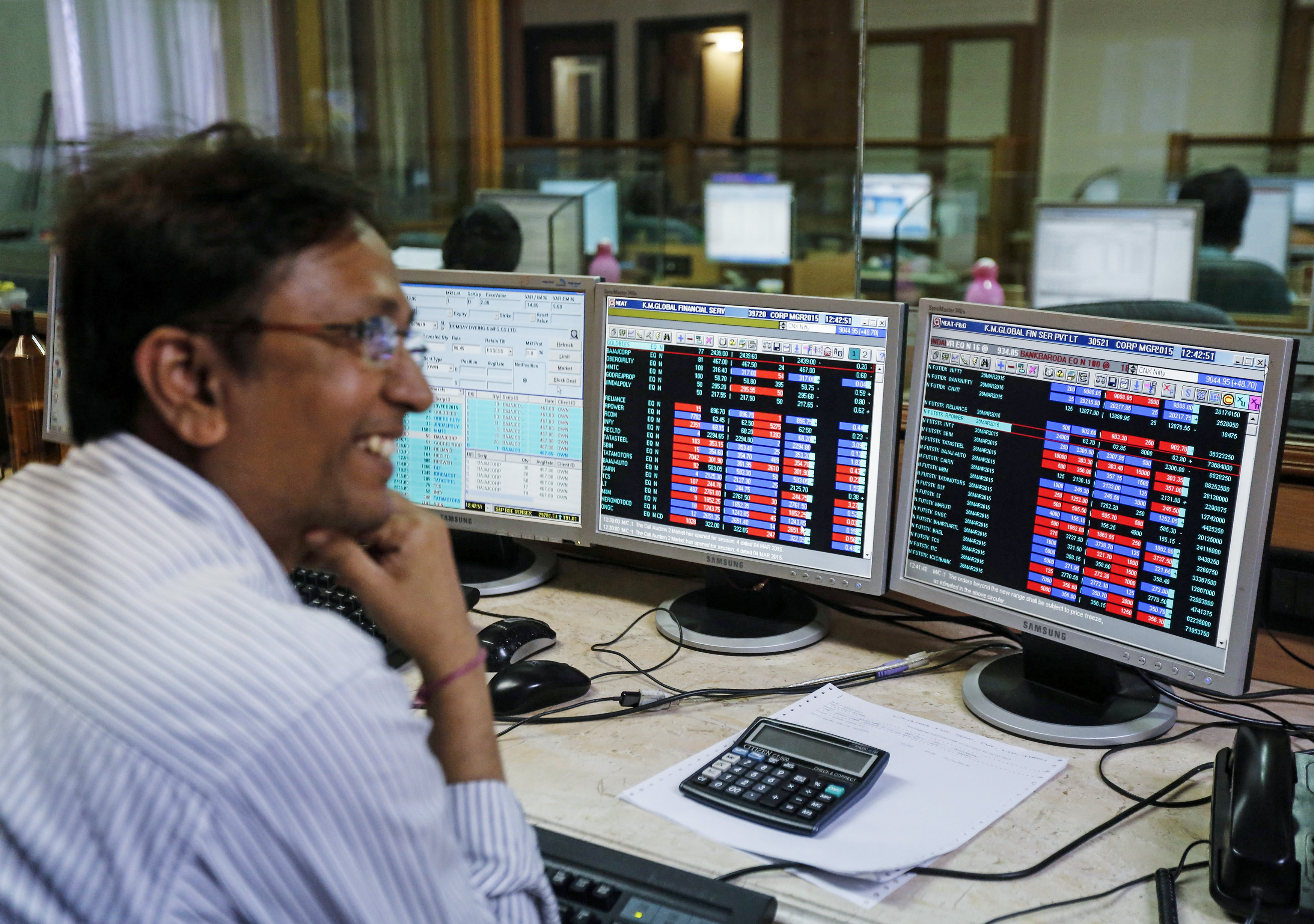 A broker laughs while speaking to a colleague, as they trade on their computer terminals at a stock brokerage firm in Mumbai