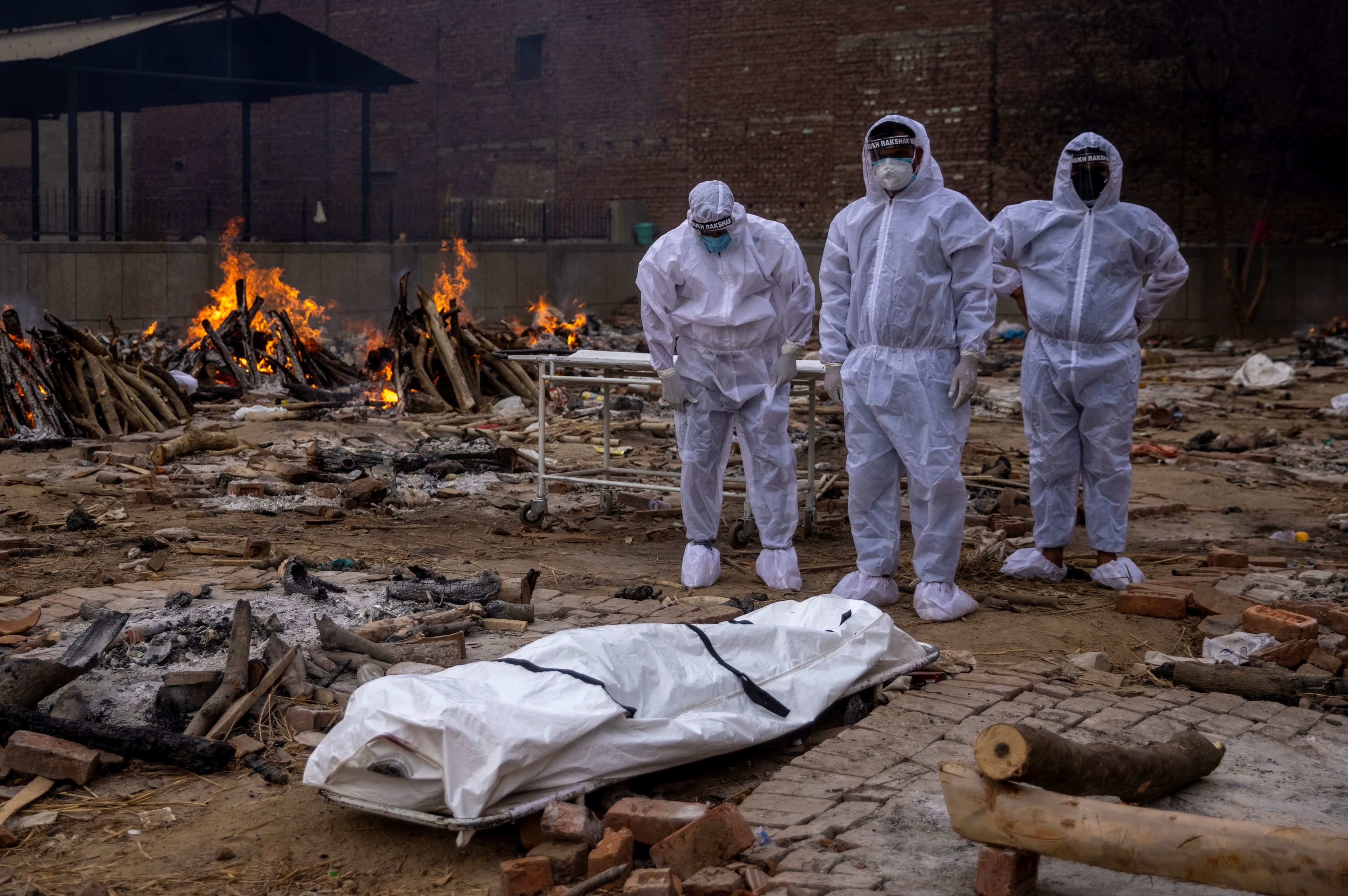 Men wearing protective suits stand next to the body of their relative, who died from the coronavirus disease (COVID-19), before her cremation at a crematorium ground in New Delhi