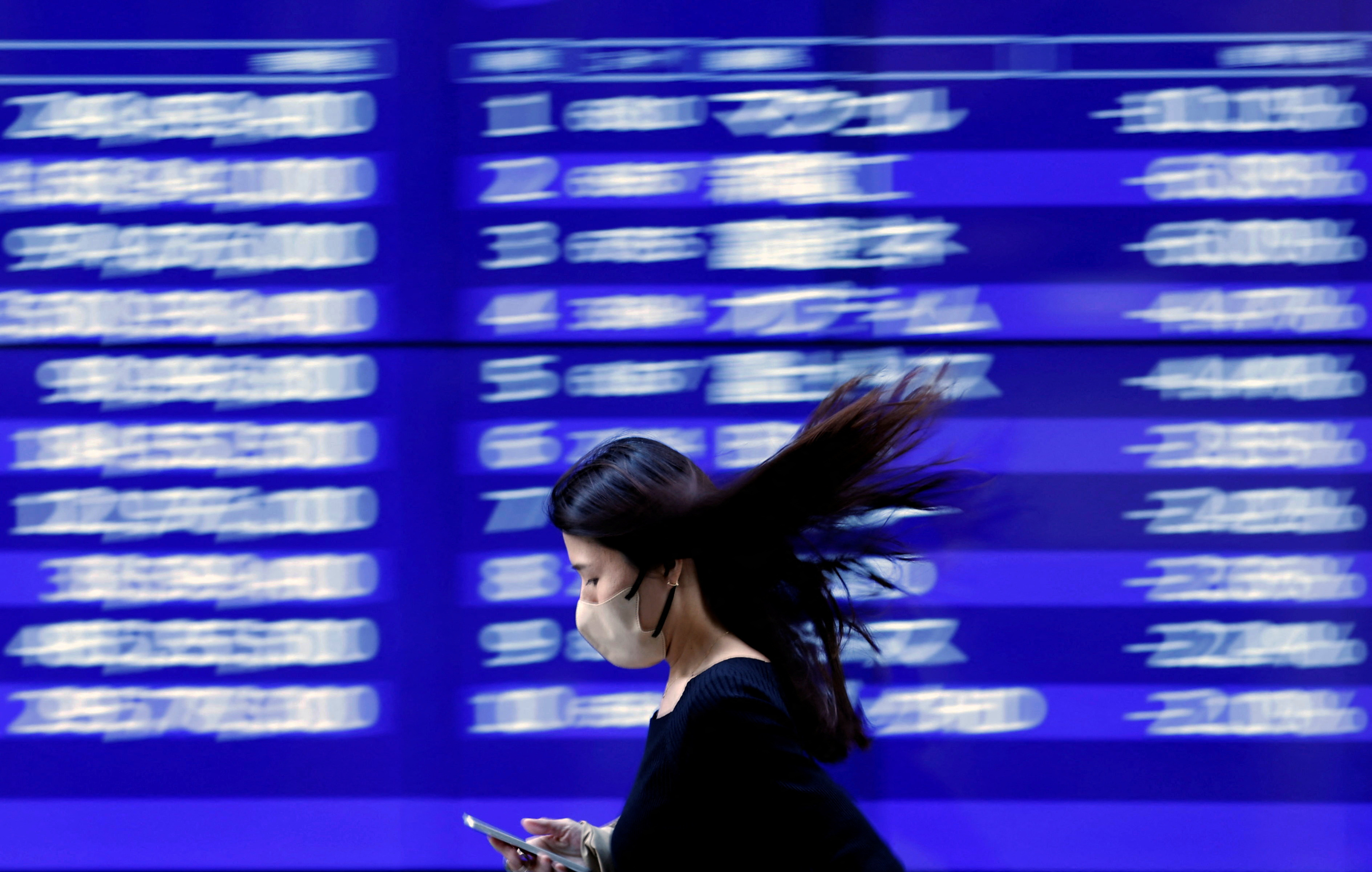 A passerby walks past an electric monitor displaying recent movements of various stock prices outside a bank in Tokyo