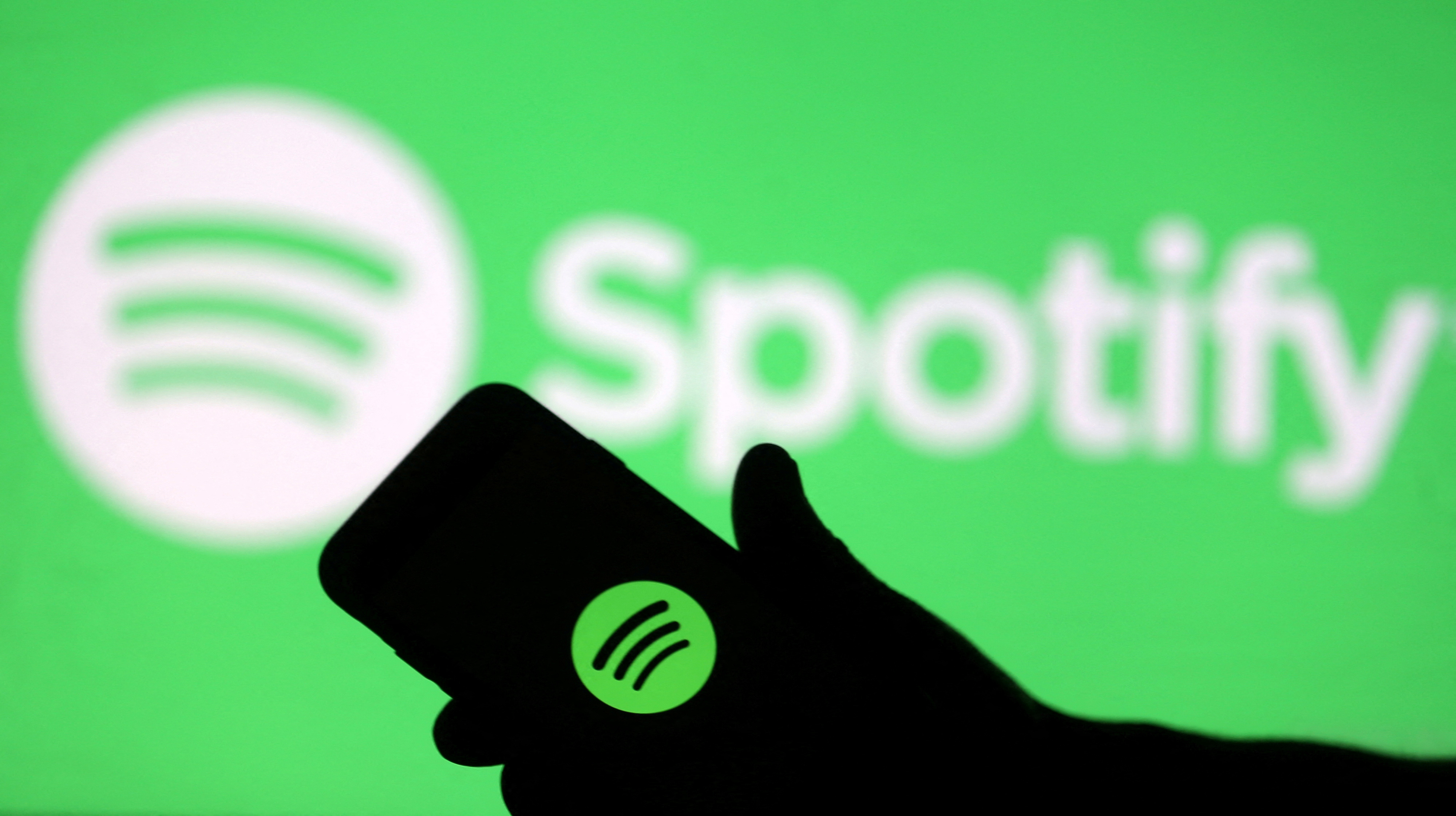 A smartphone is seen in front of a screen projection of the Spotify logo in this picture illustration