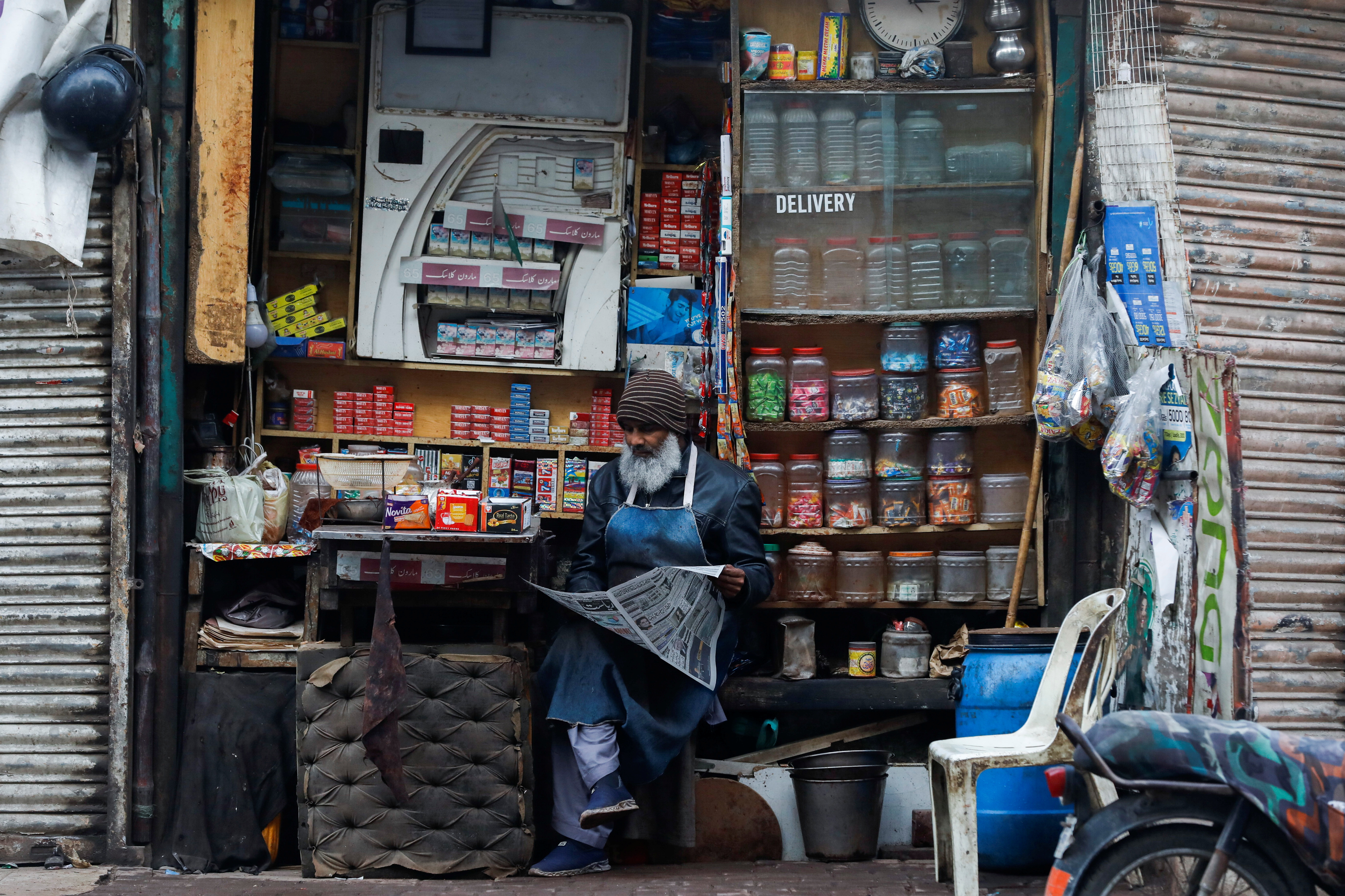 A man reads newspaper while selling betel leaves, cigarettes and candies from a shop in Karachi