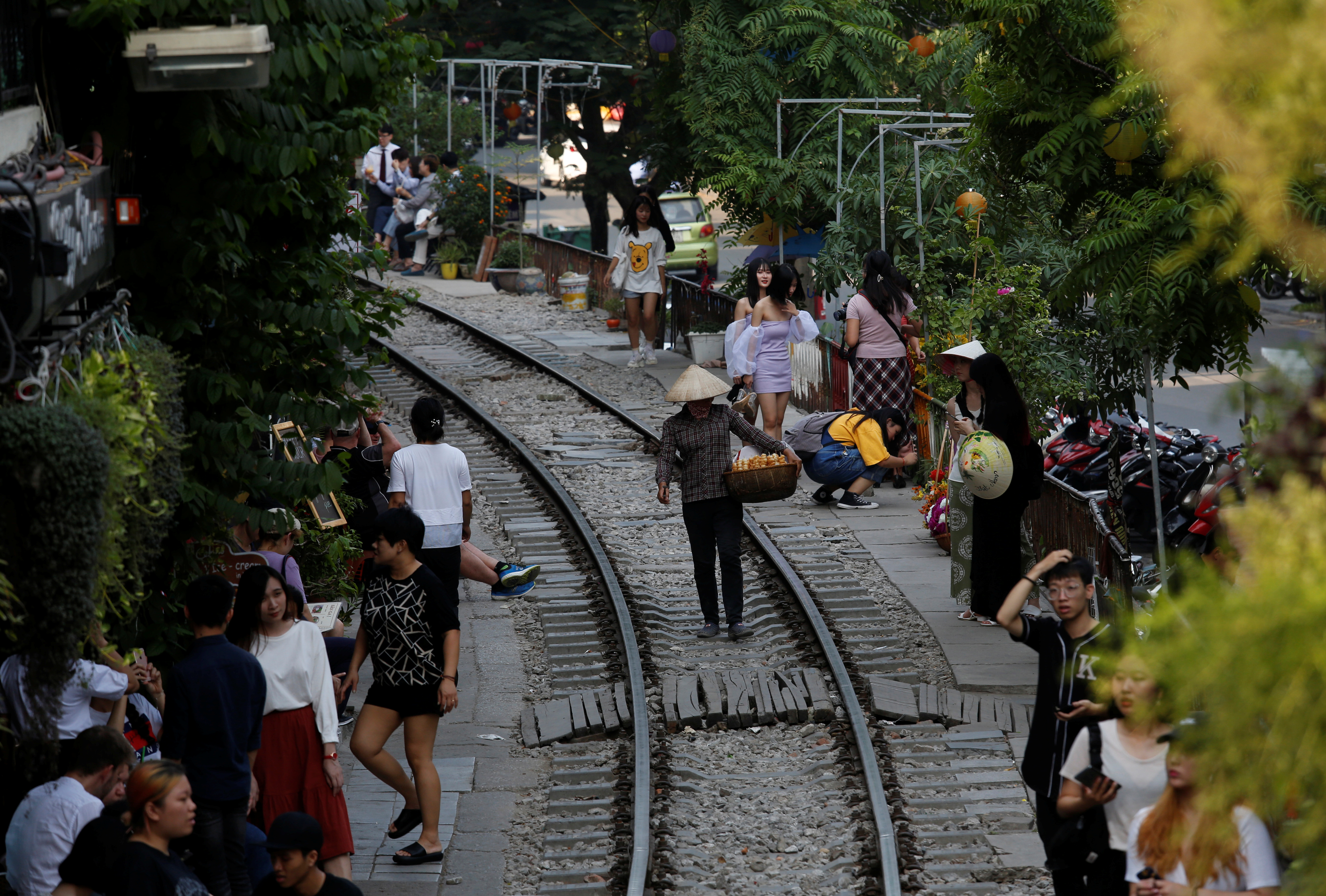 A vendor walks on a railway track as tourists gather on either side, in the Old Quarter of  Hanoi, Vietnam