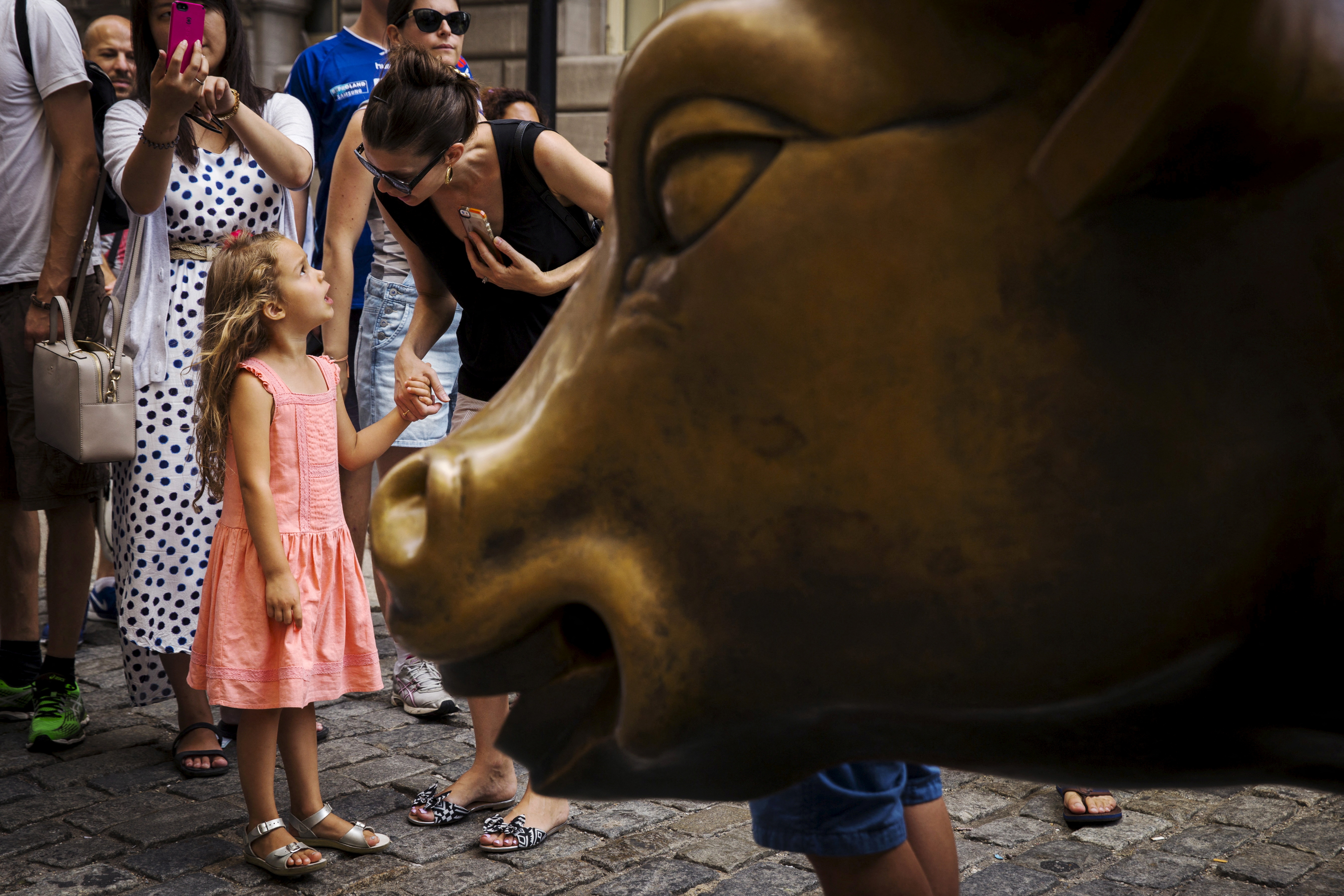 A girl speaks with her mother near a landmark statue of a bull in New York