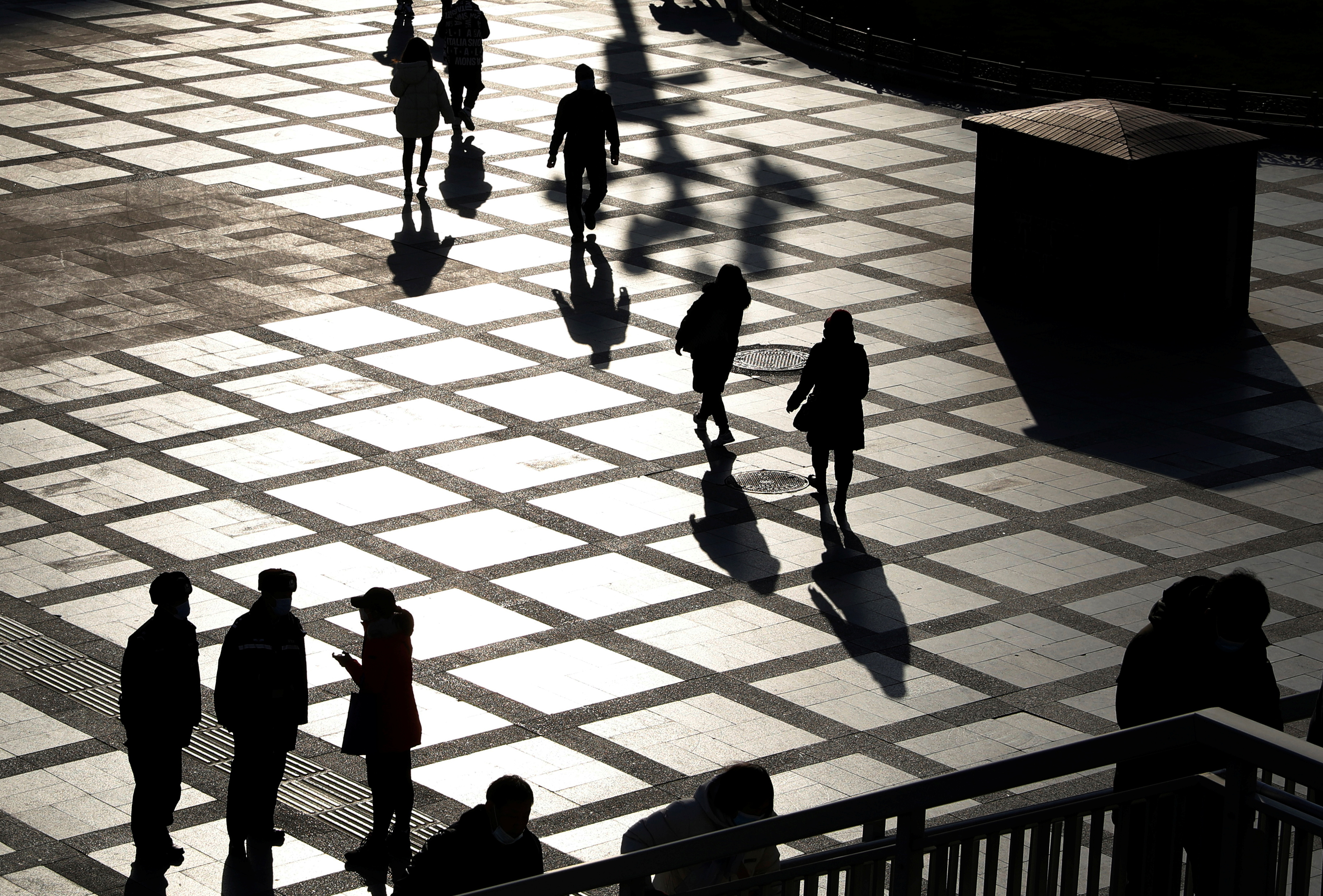 People are seen in silhouette on a street on a winter day in Beijing