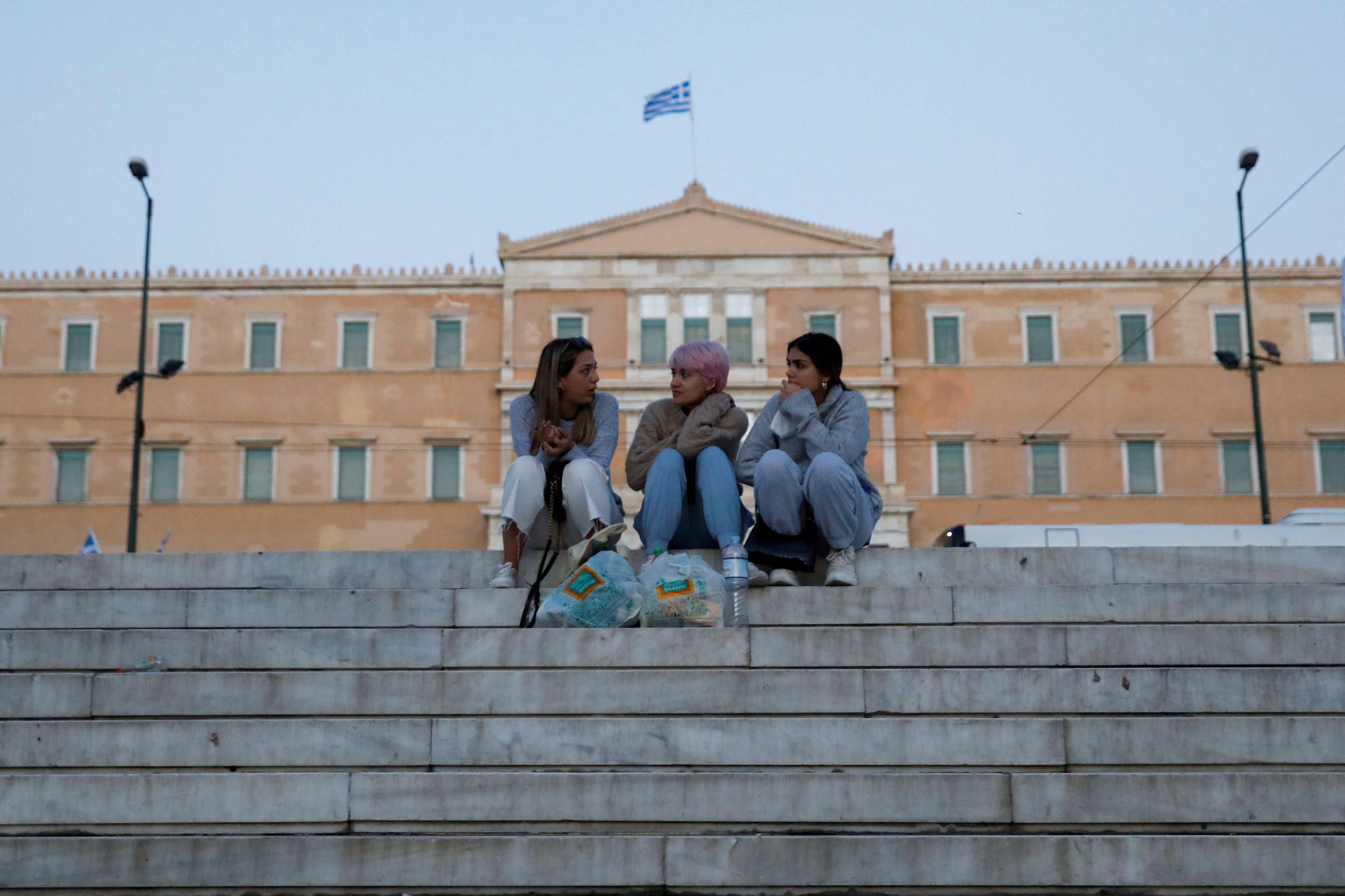 People sit at Syntagma square where parliament building is seen in the background, in Athens