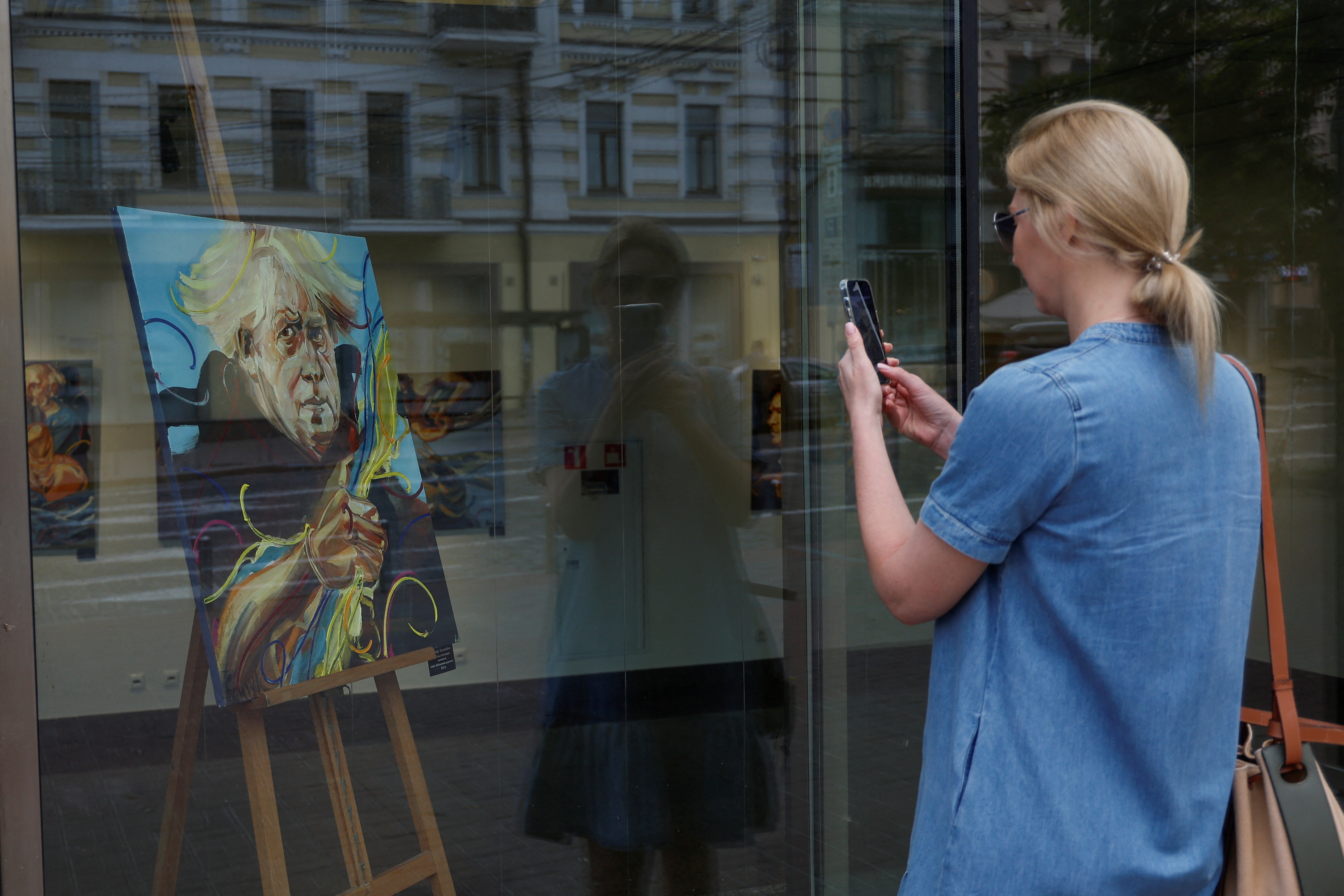 A woman takes a picture of a portrait of British Prime Minister Boris Johnson displayed at a gallery in Kyiv