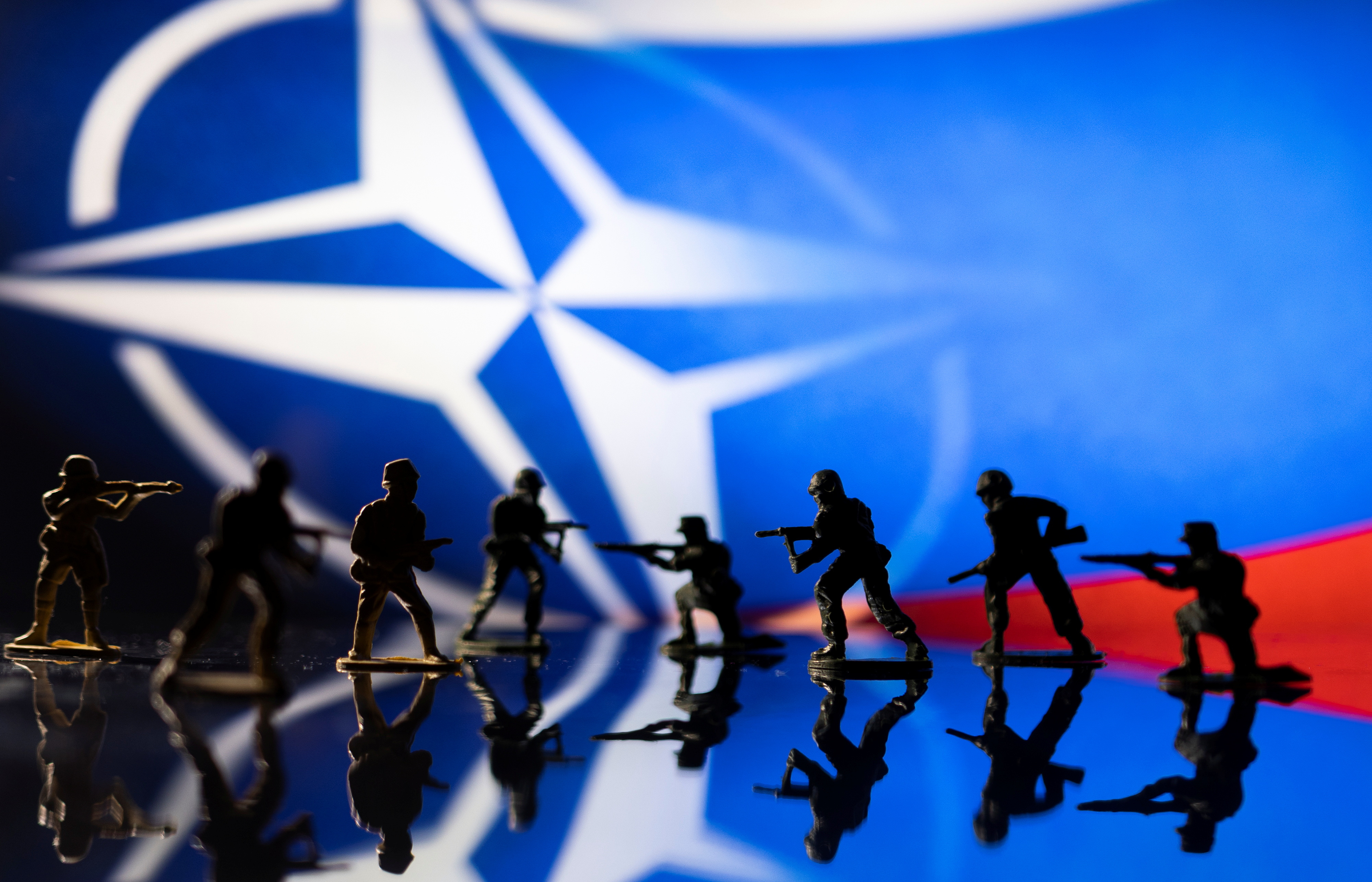 Illustration shows army figurines on NATO logo and Russian flag colours background