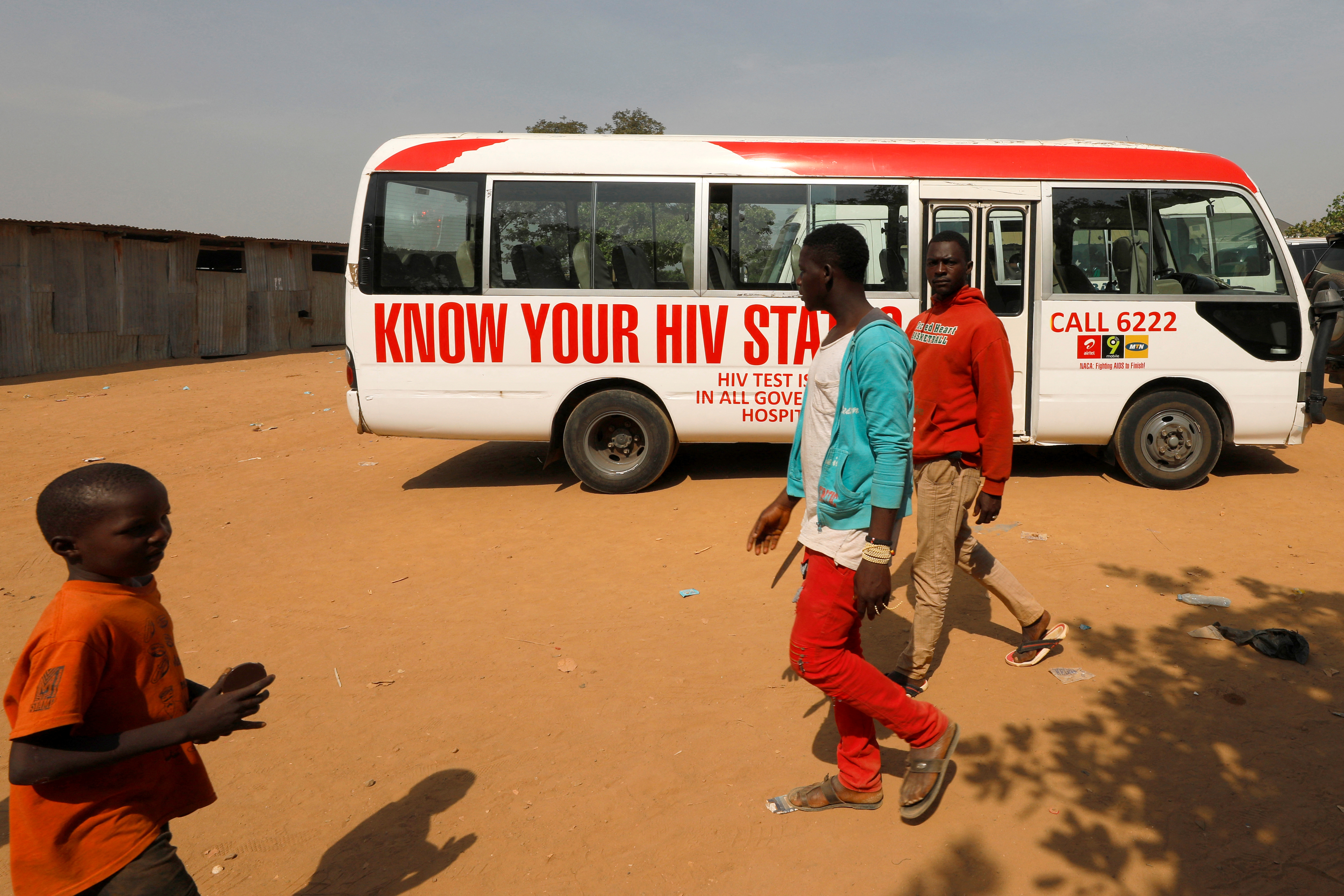 People walk past a bus during an HIV/AIDS awareness campaign on the occasion of World AIDS Day at the Kuchingoro IDPs camp in Abuja
