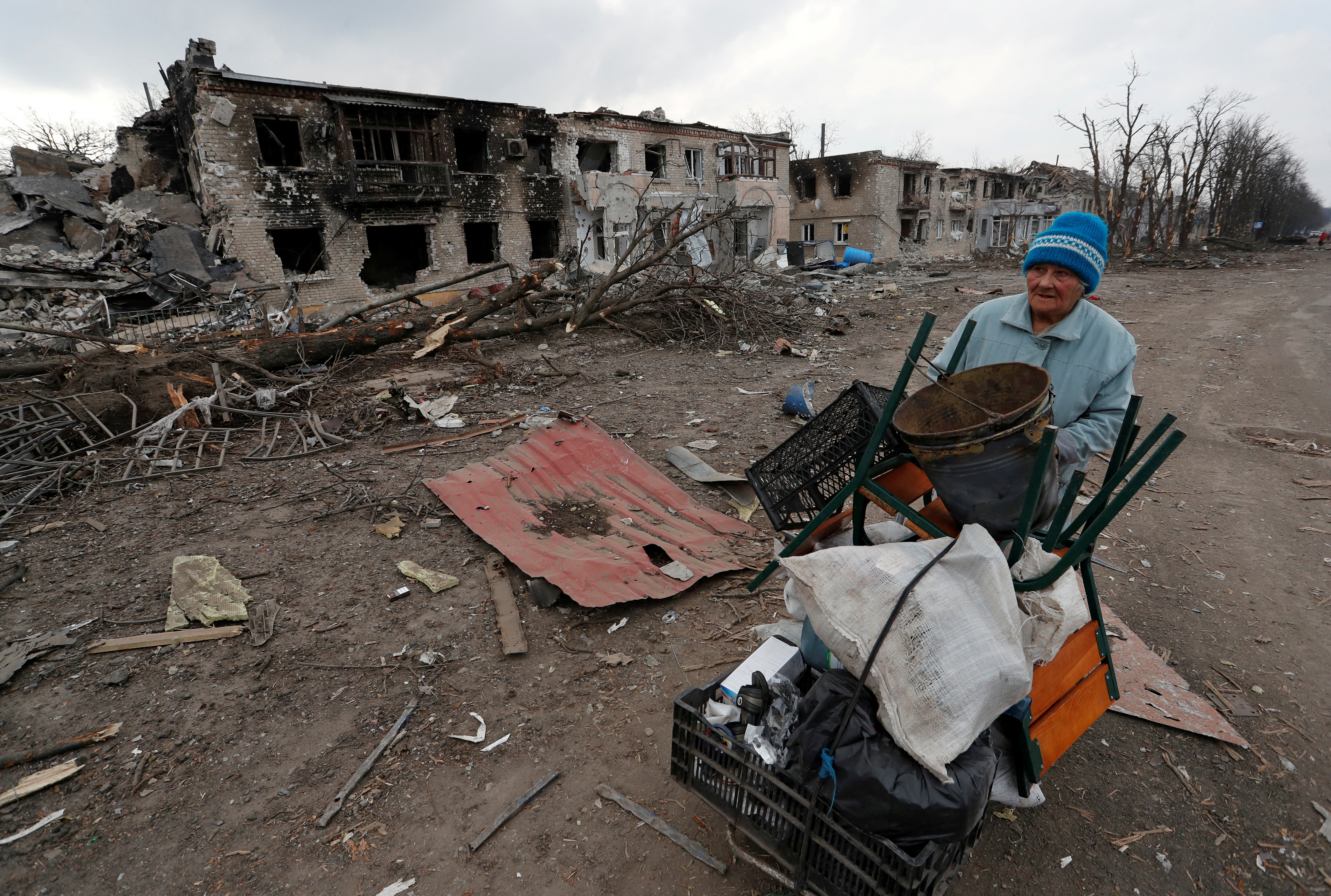 A woman pushes a trolley with her belongings along a damaged street in Volnovakha