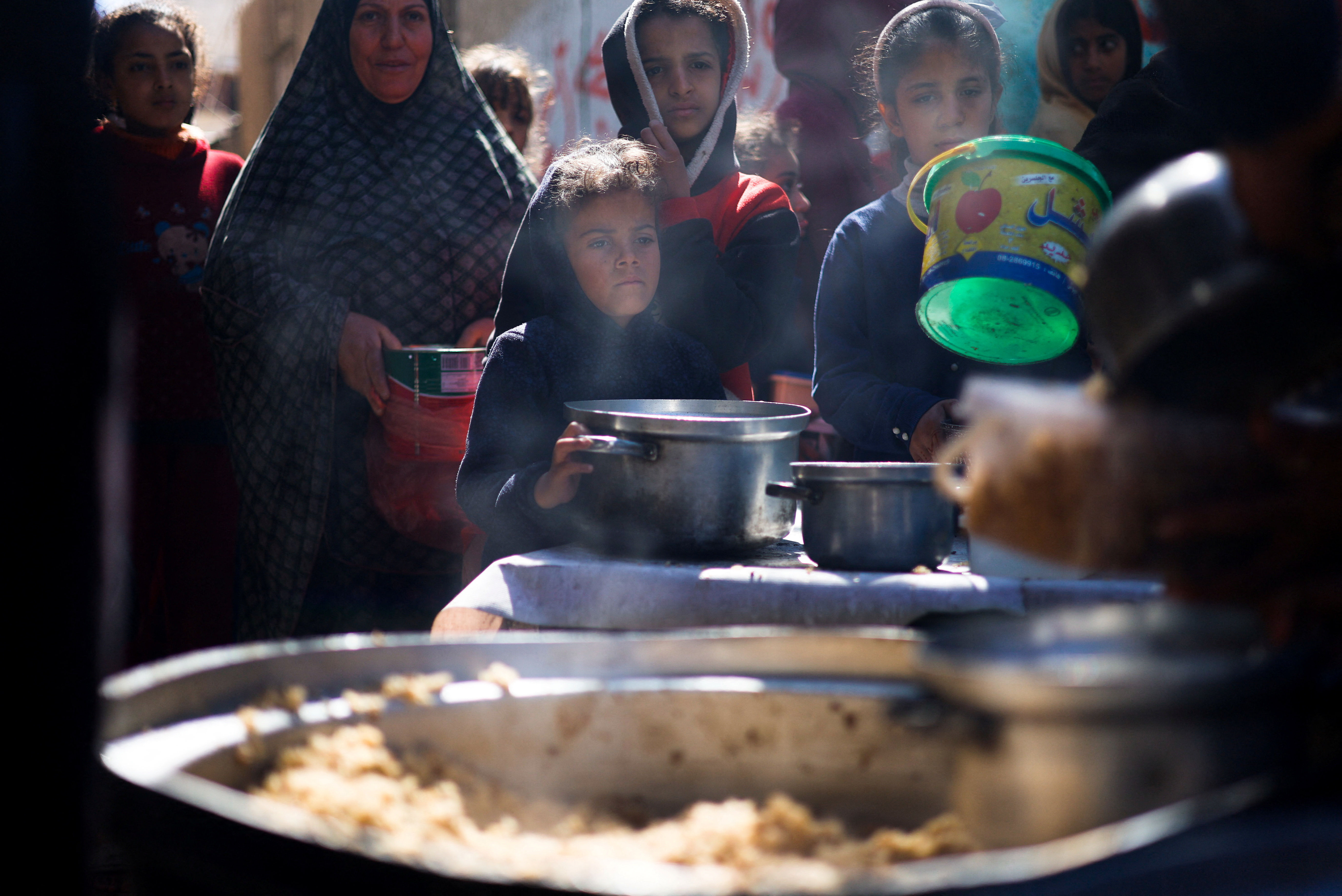 Palestinian children wait to receive food cooked by a charity kitchen amid shortages of food supplies, in Rafah